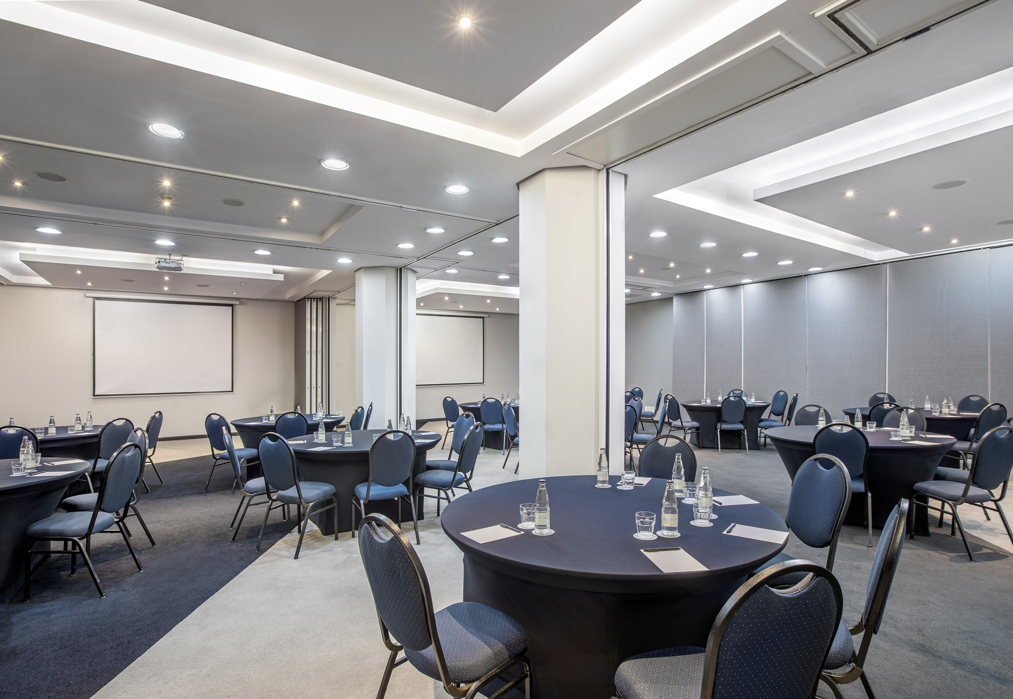 Hotel conference room with multiple round tables, chairs, and presentation screens.