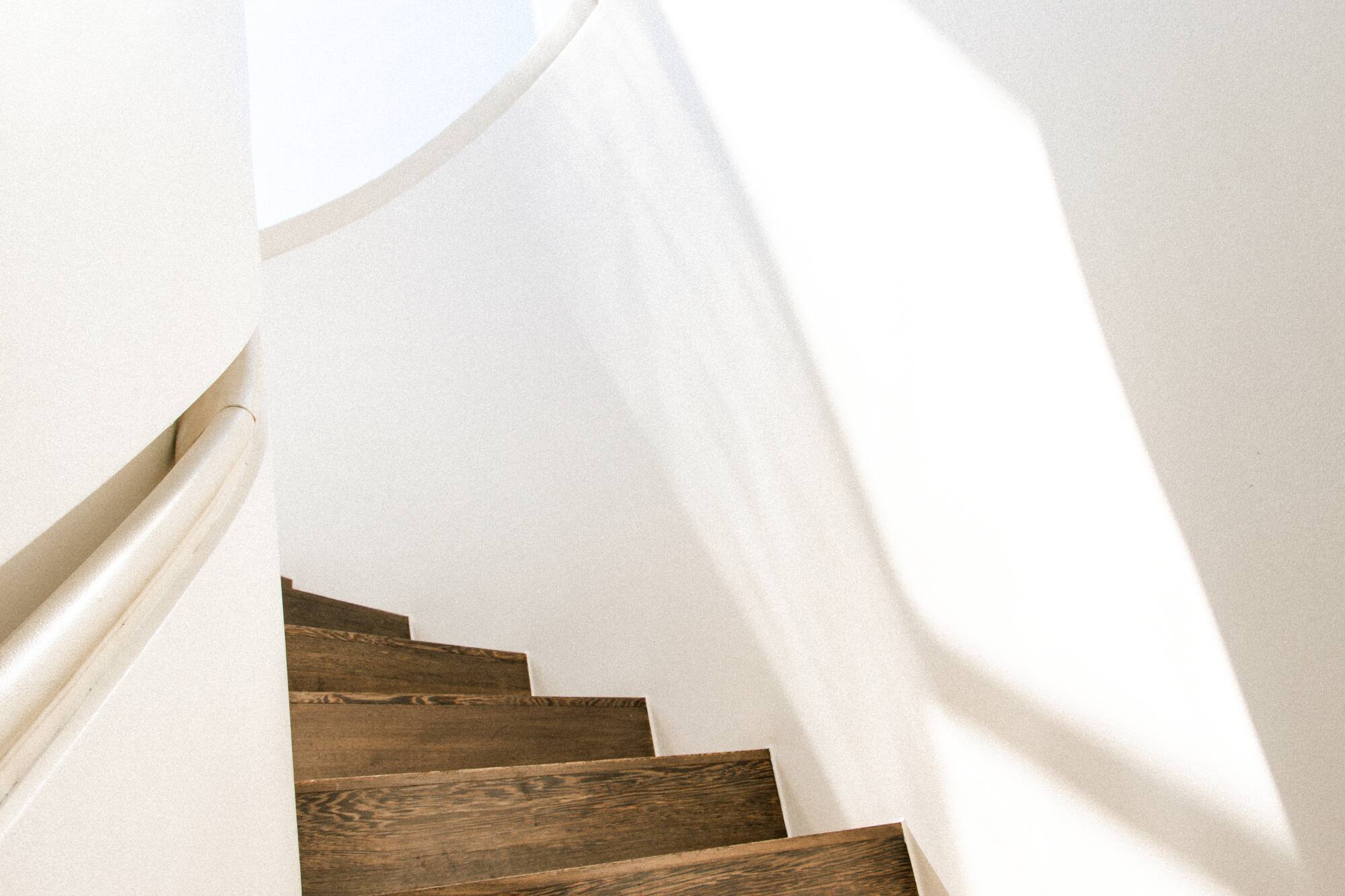 Sunlit dark wood spiral staircase, white walls, modern interior design.