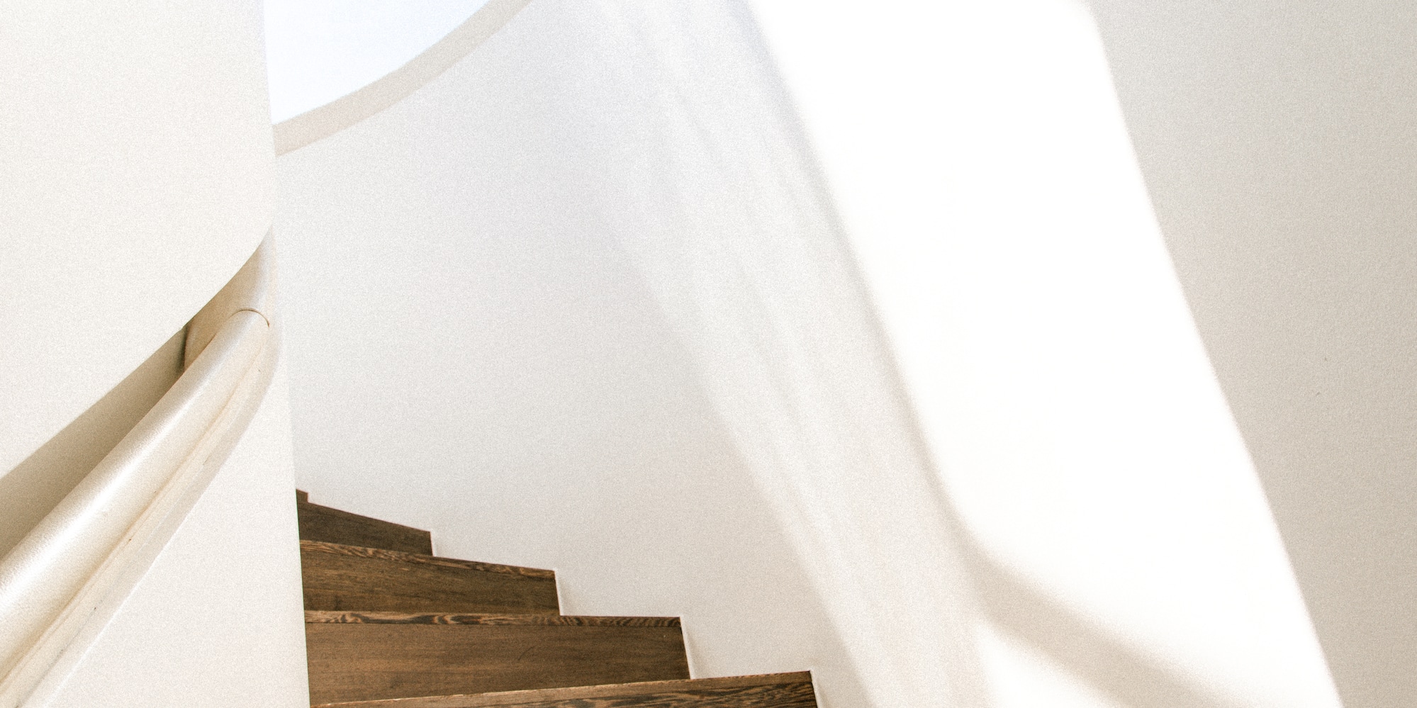 Sunlit dark wood spiral staircase, white walls, modern interior design.