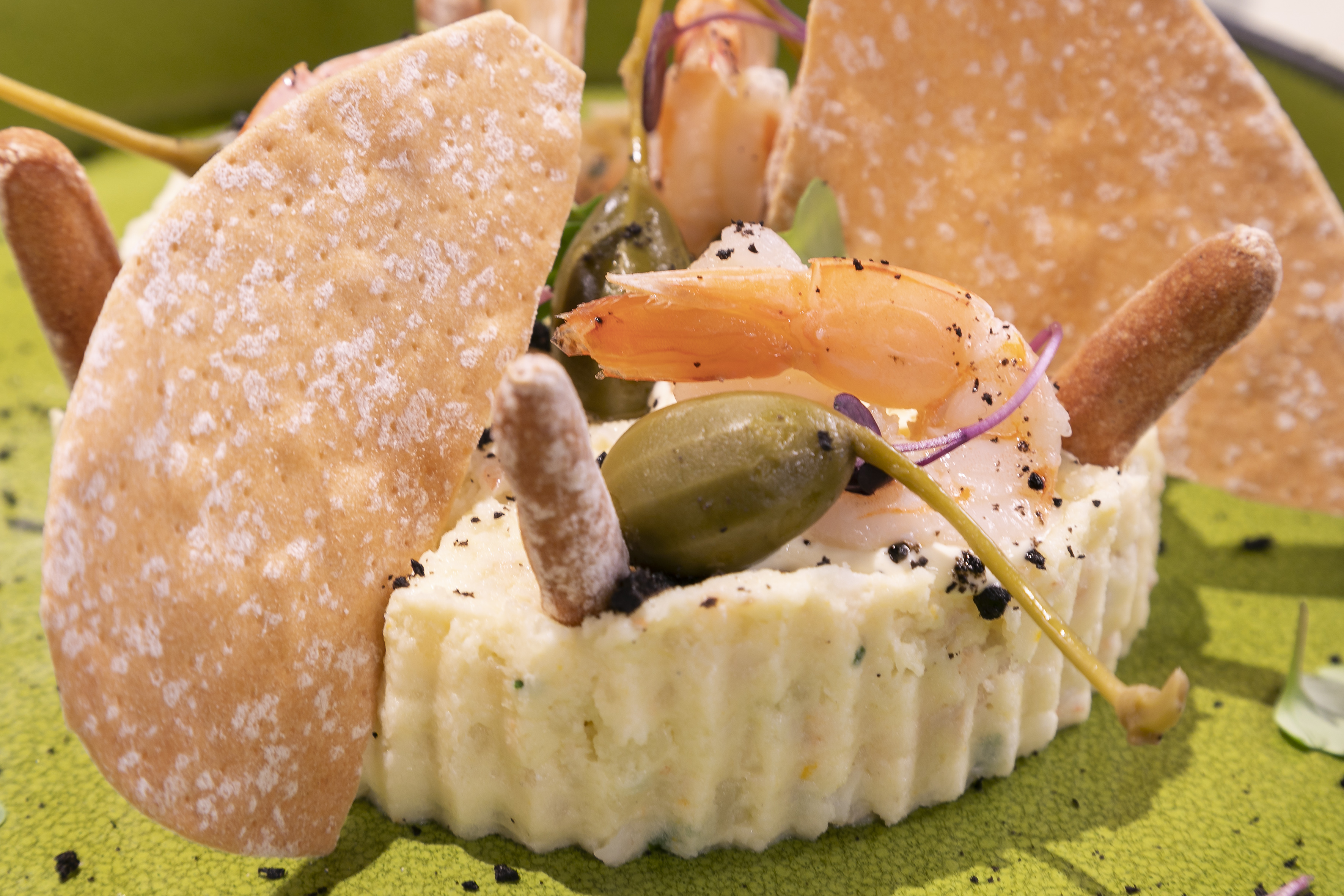 Seafood potato salad with shrimp, capers, and crackers on a green plate.