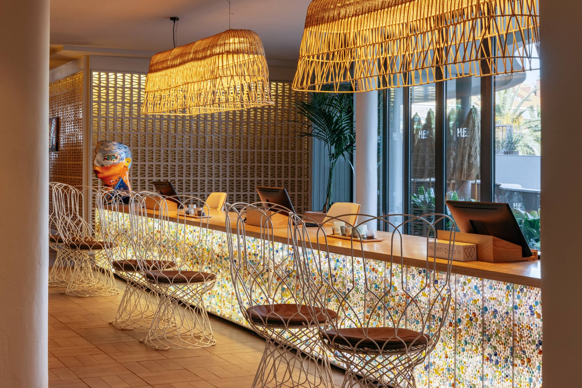 Colorful hotel reception with unique counter, modern stools, and rattan lights.