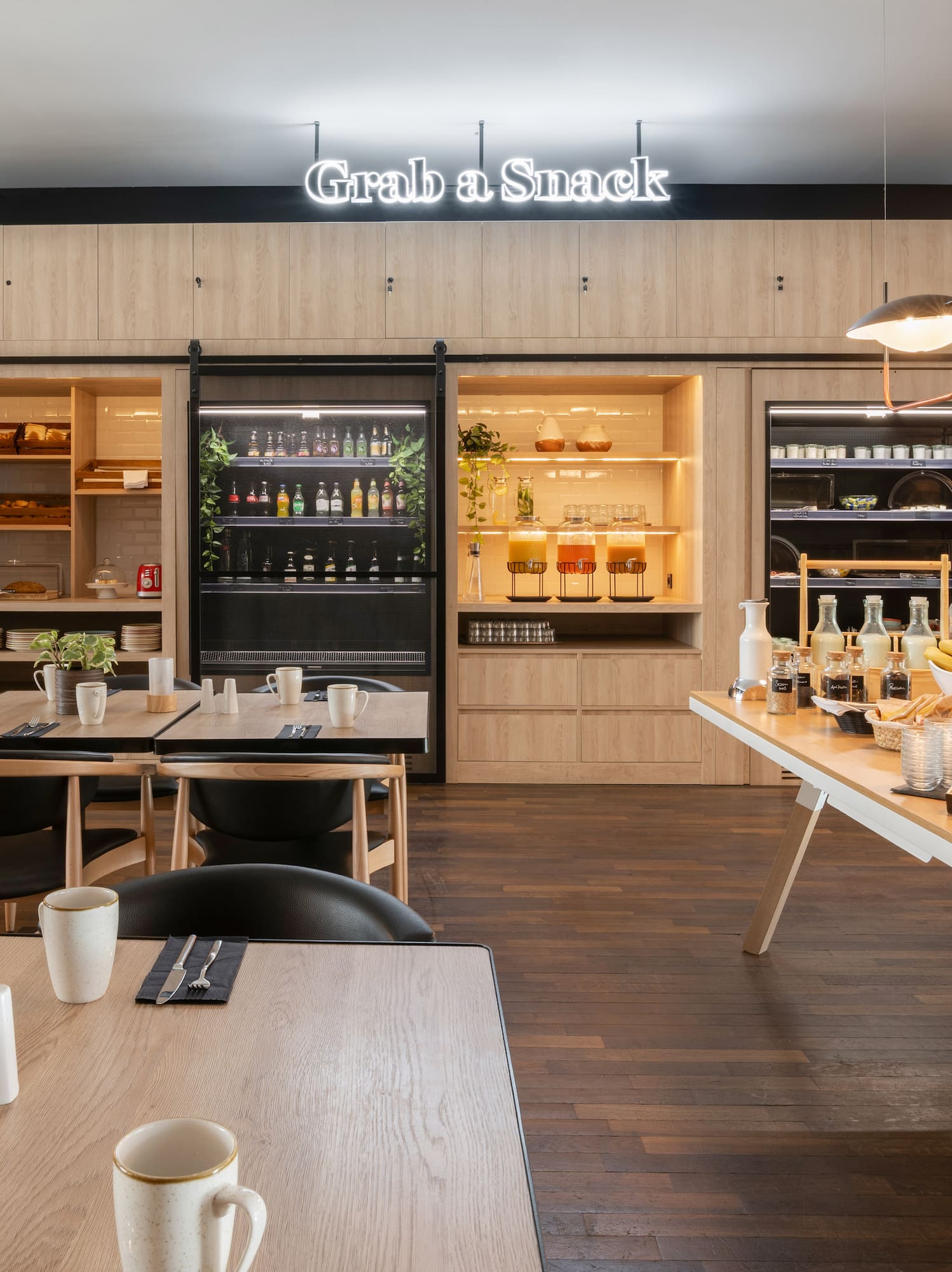 Modern hotel snack bar with self-service buffet, drinks, and dining tables.