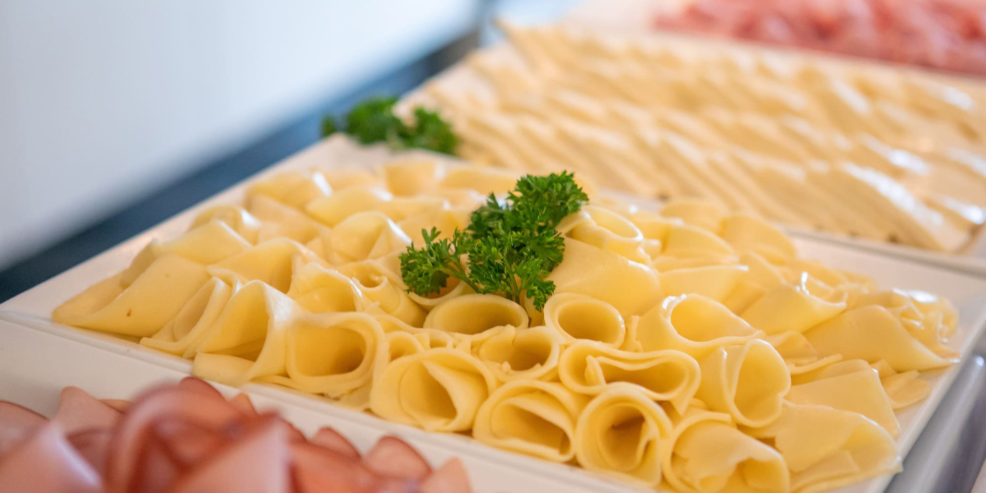 Rolled yellow cheese slices with parsley on a buffet. Deli meats.