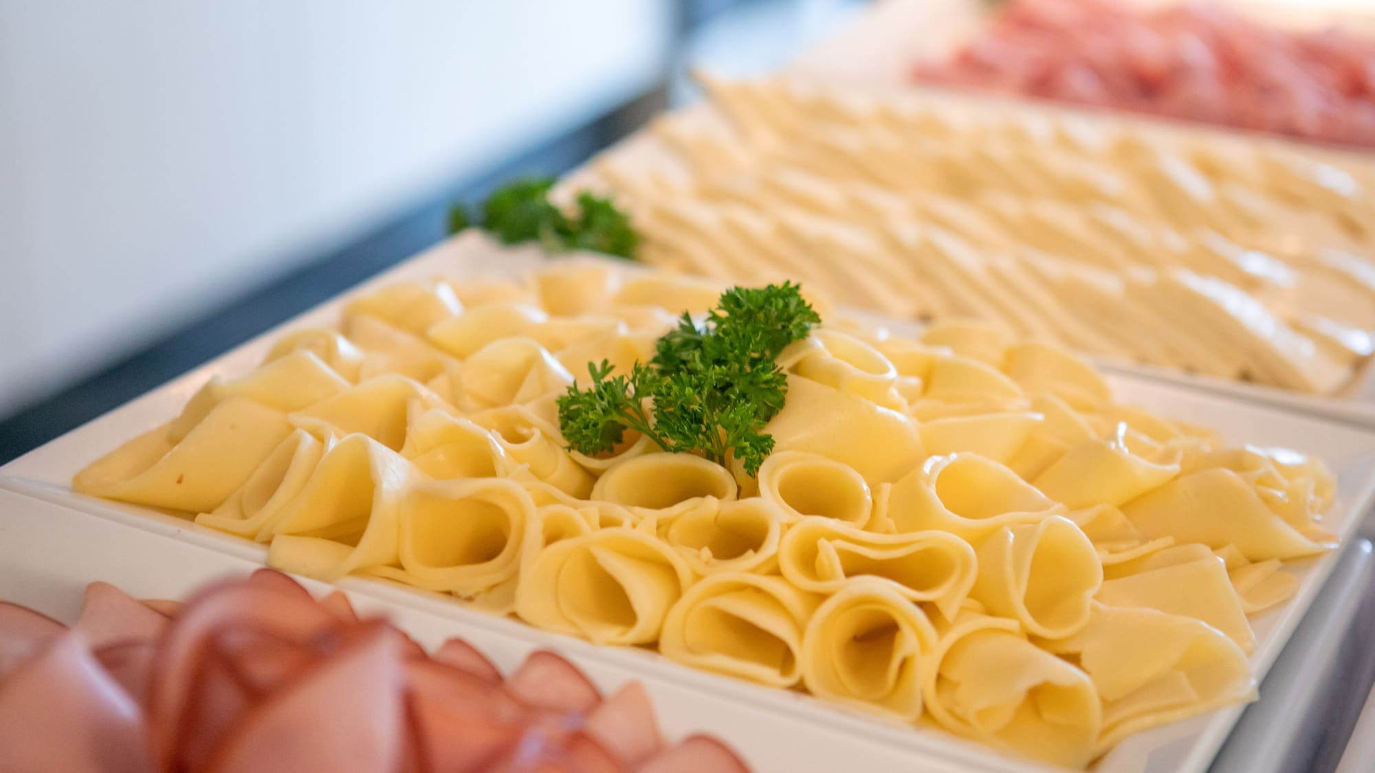Rolled yellow cheese slices with parsley on a buffet. Deli meats.