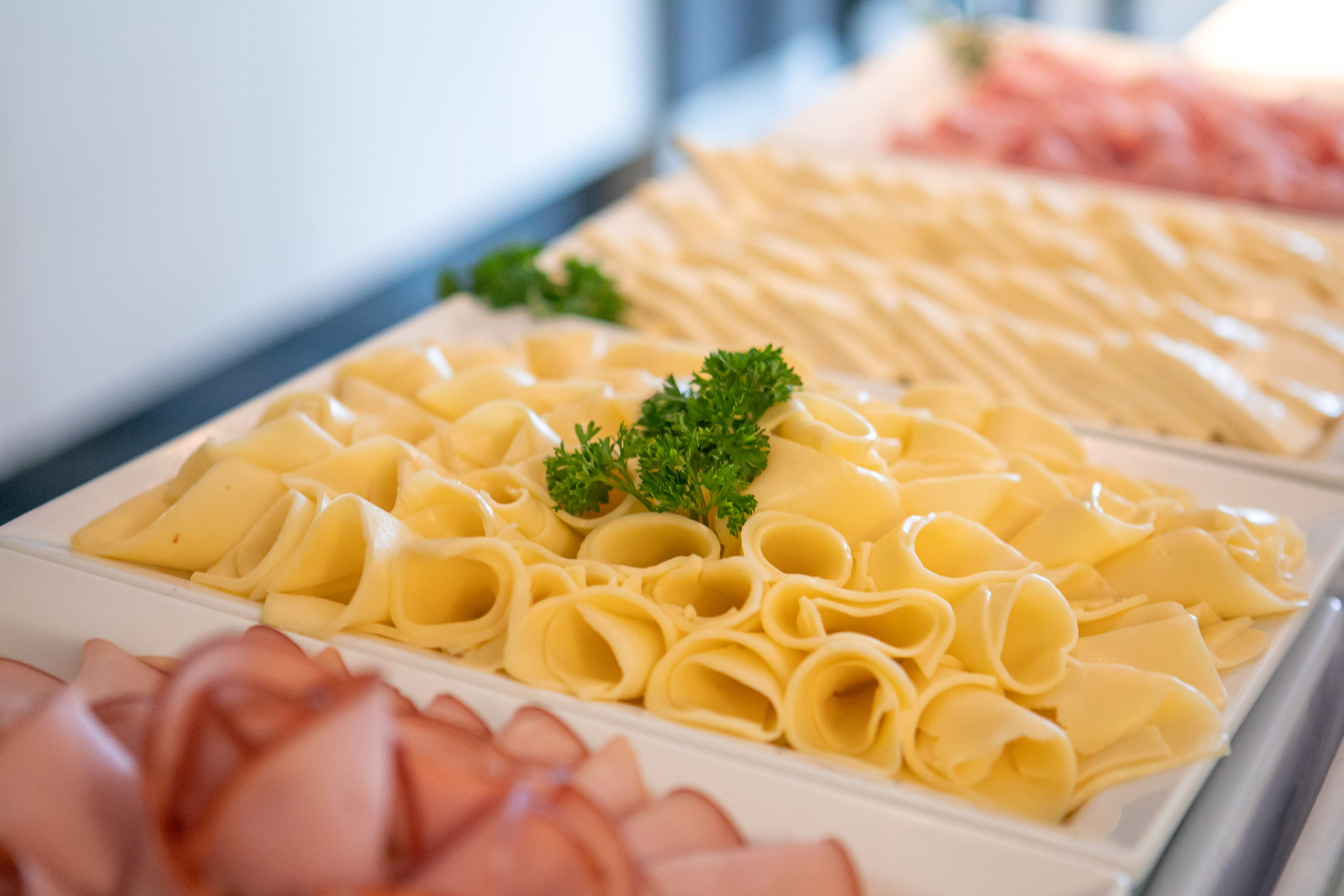 Rolled yellow cheese slices with parsley on a buffet. Deli meats.