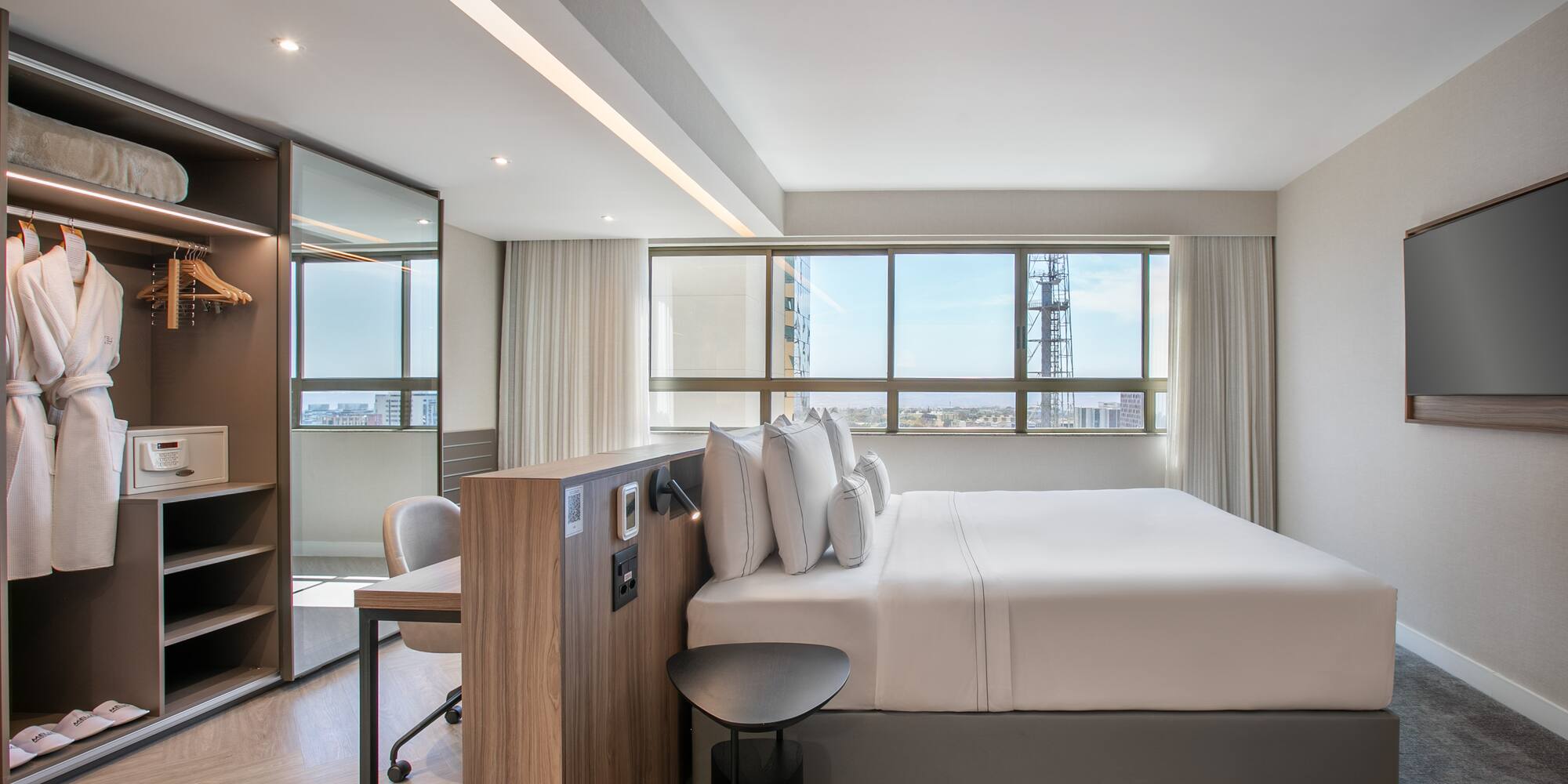 Modern hotel room with comfortable bed, city view window, and desk workspace.