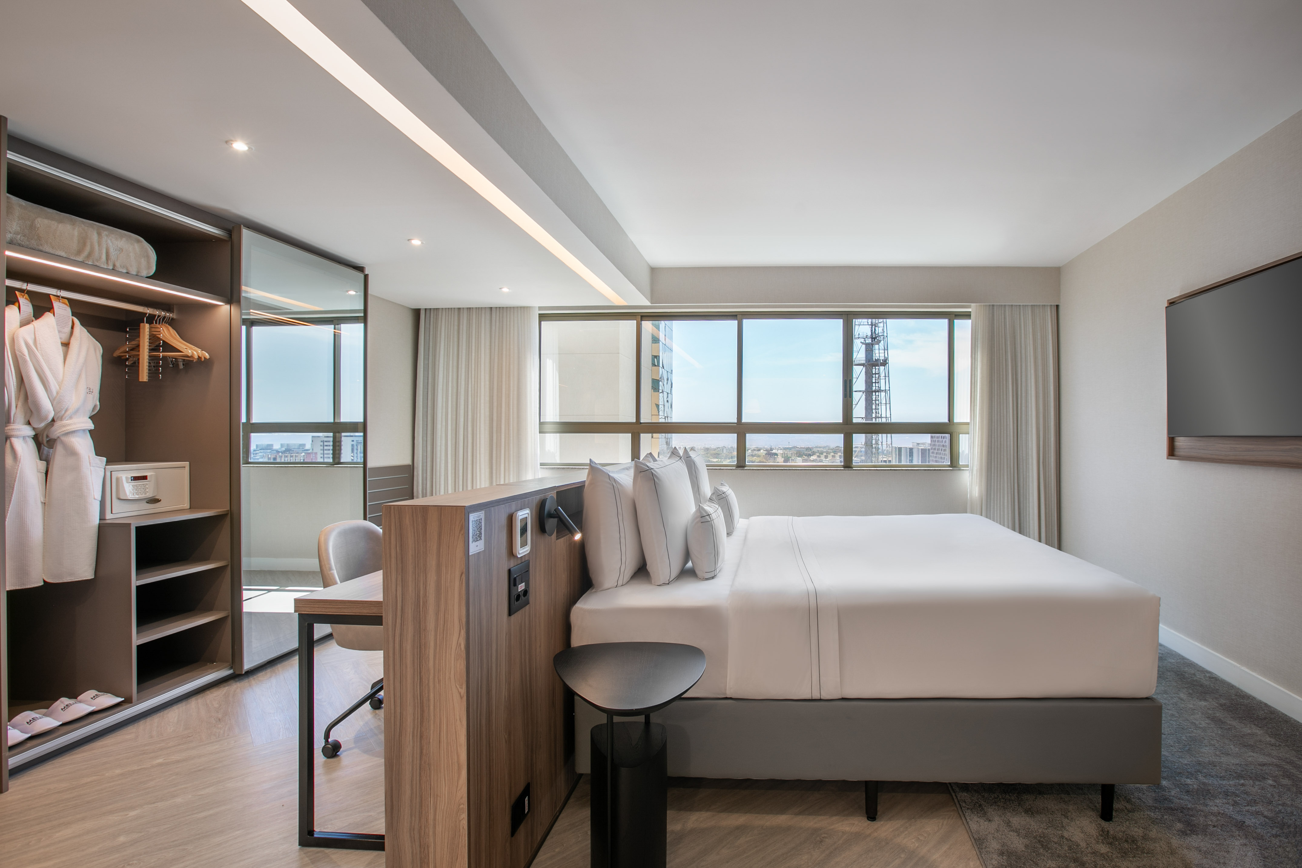 Modern hotel bedroom with city view, king bed, desk, and open closet.
