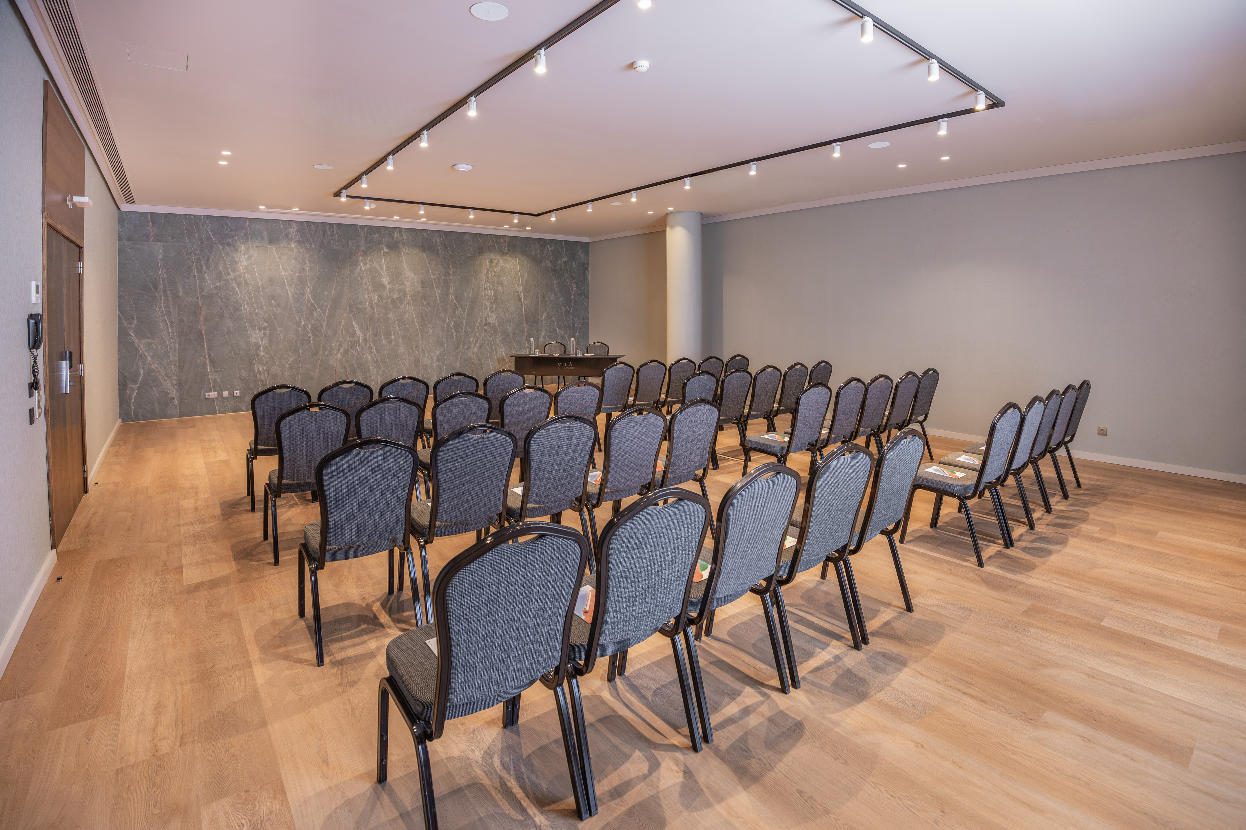 Hotel meeting room with grey chairs, wooden floor, and marble accent wall.