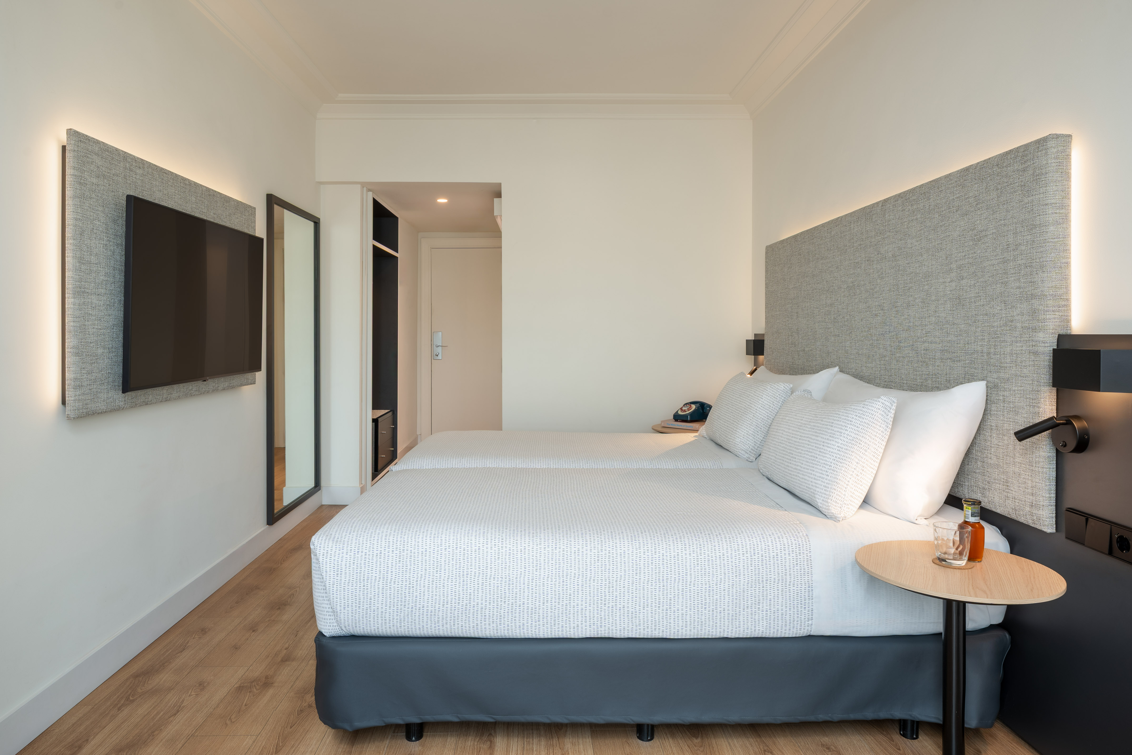Dormitorio de hotel moderno con dos camas individuales, TV y cabeceros retroiluminados.