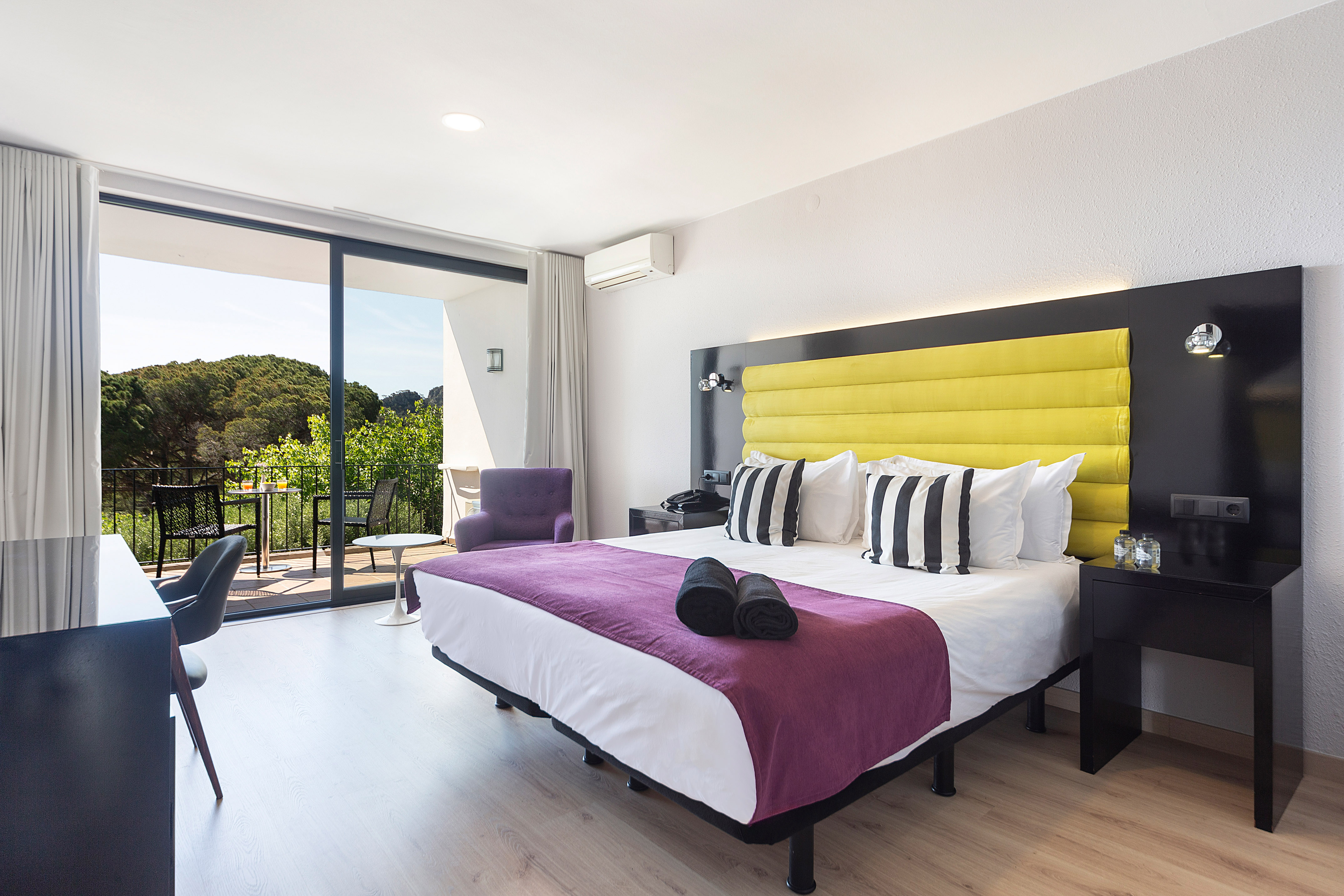 Modern hotel room with yellow bed, purple runner, balcony, and forest view.