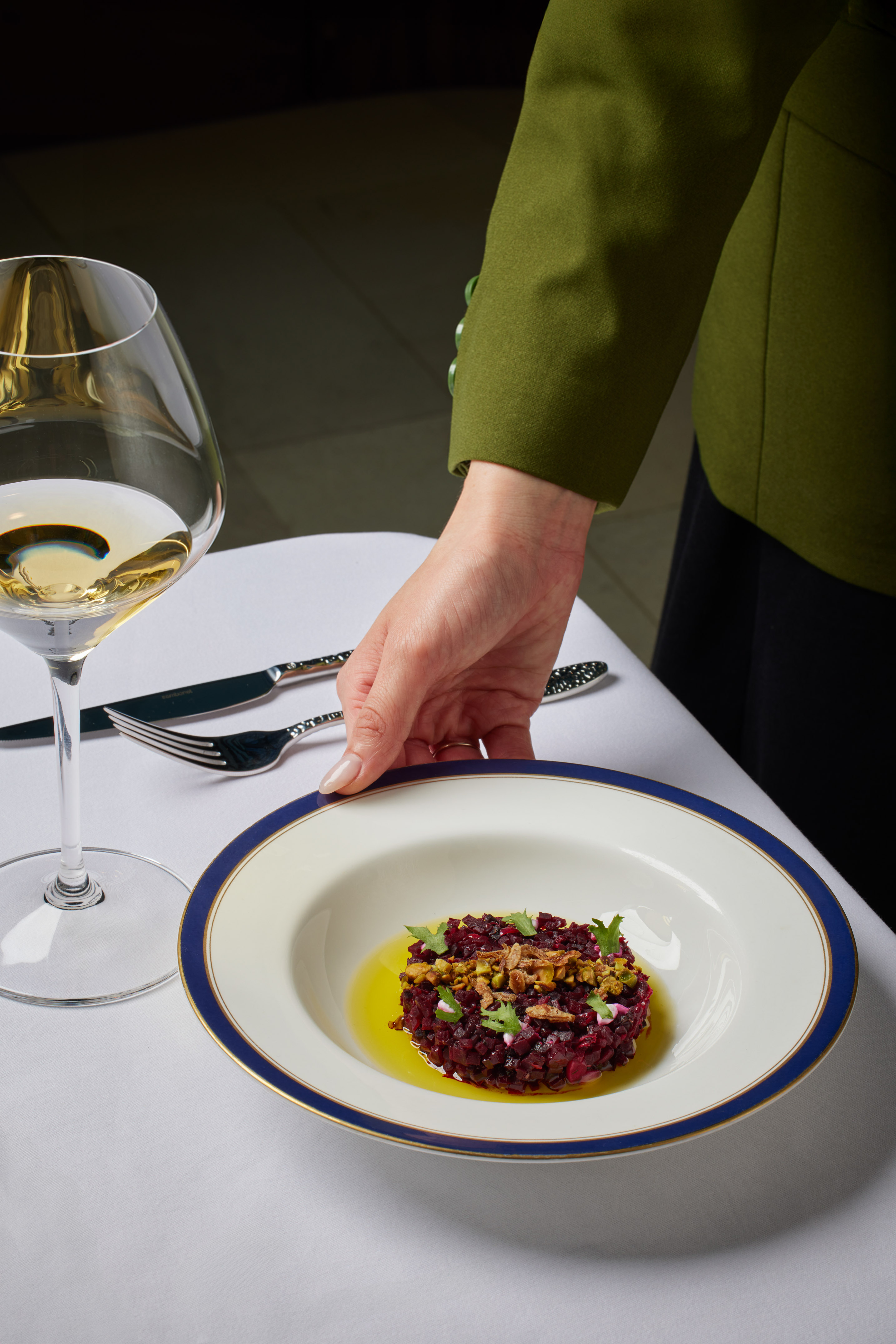 Hand serving elegant beet tartare with white wine on a fine dining table.