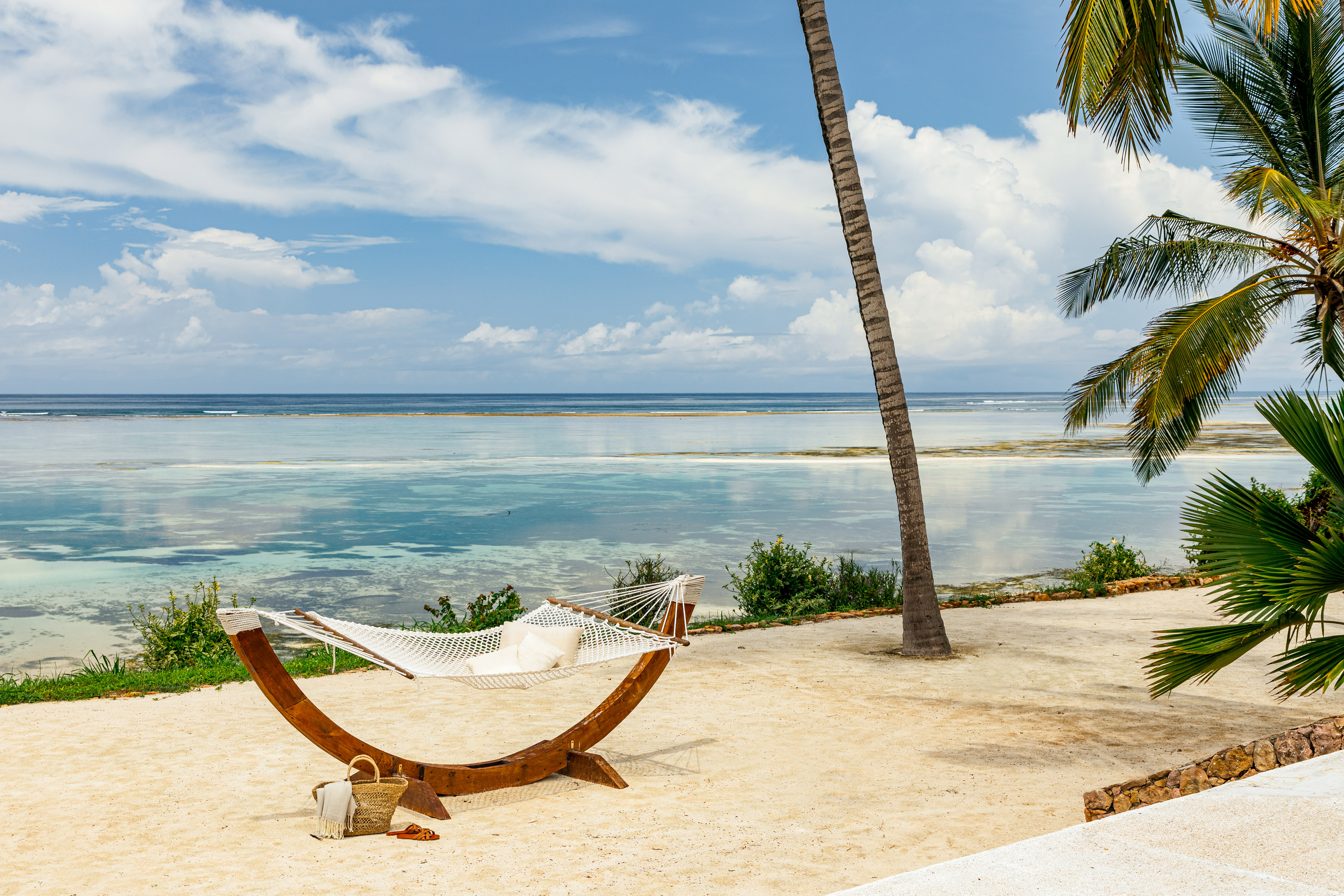 Tropical beach with white hammock, palm trees, and clear turquoise ocean.