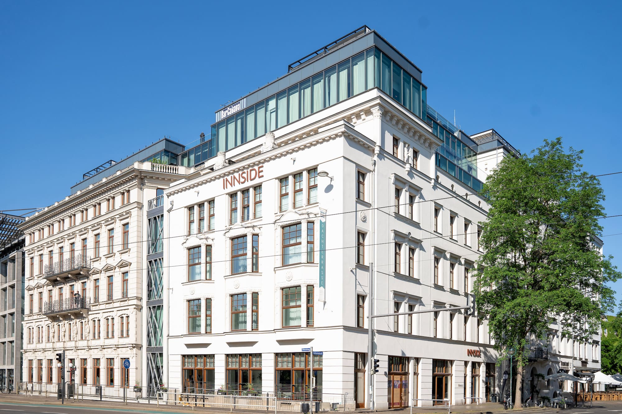 Innside hotel: white building with traditional facade and modern glass rooftop, blue sky.