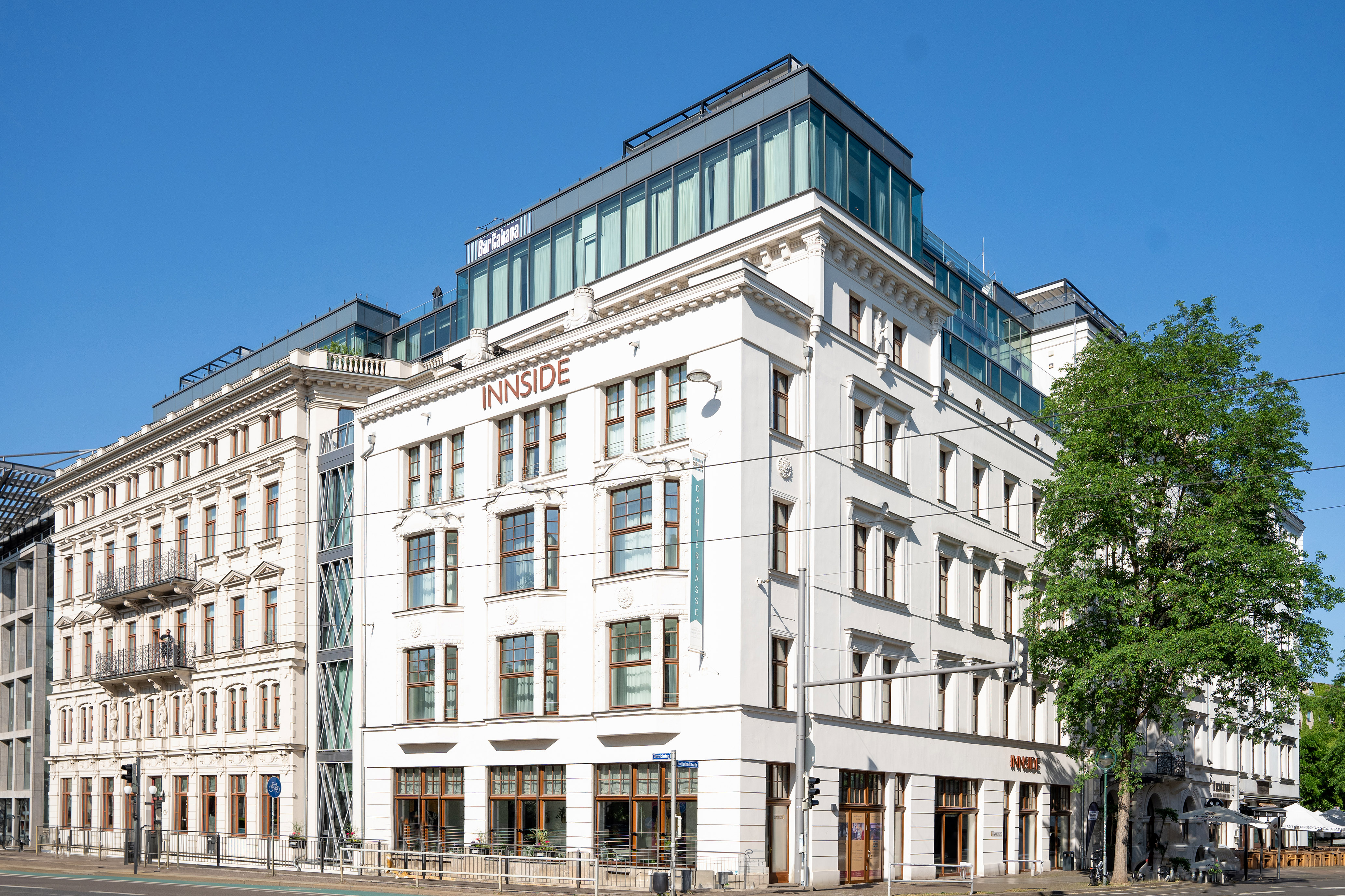 Innside hotel: white building with traditional facade and modern glass rooftop, blue sky.
