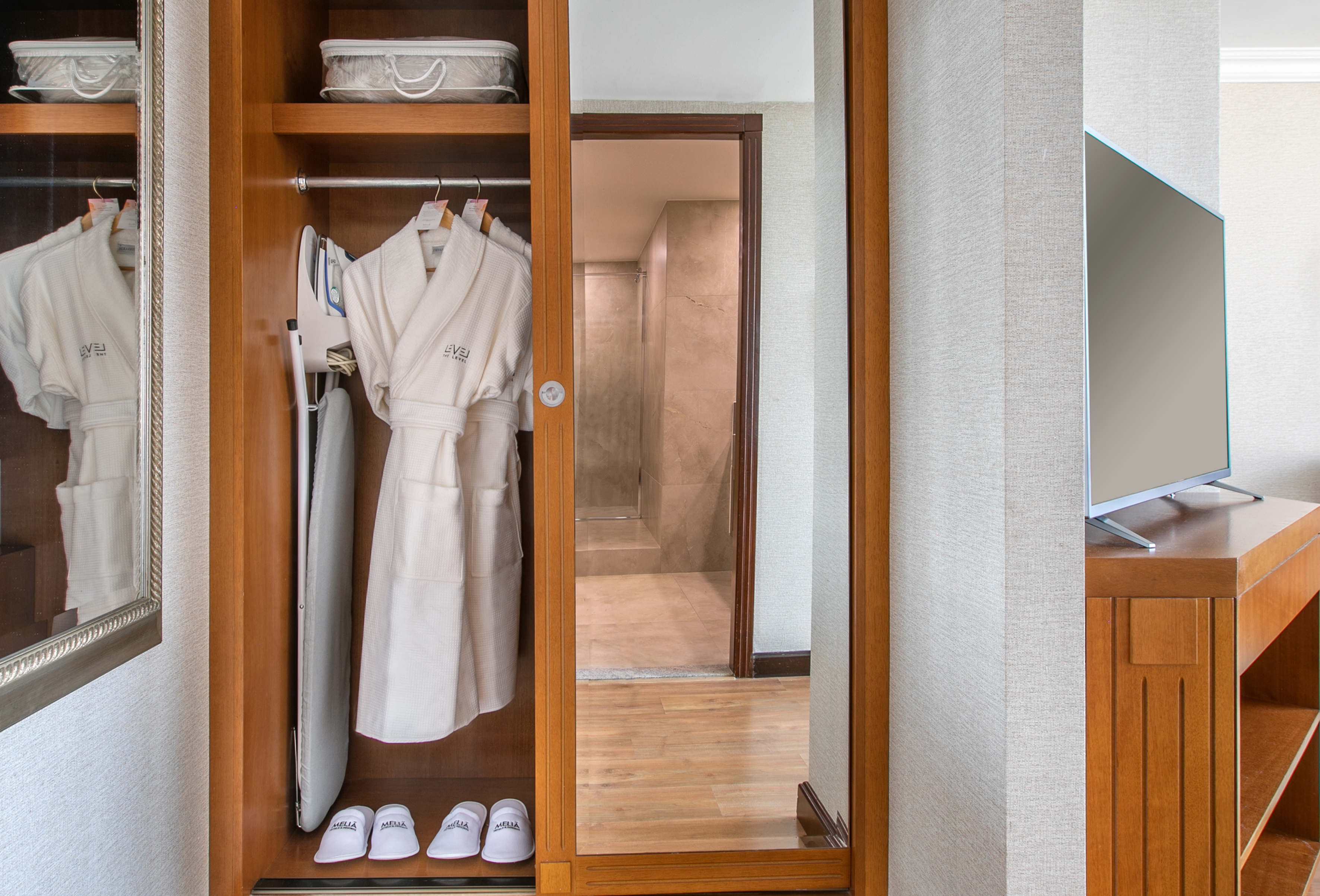 Hotel room closet: white bathrobes, iron, ironing board, slippers.