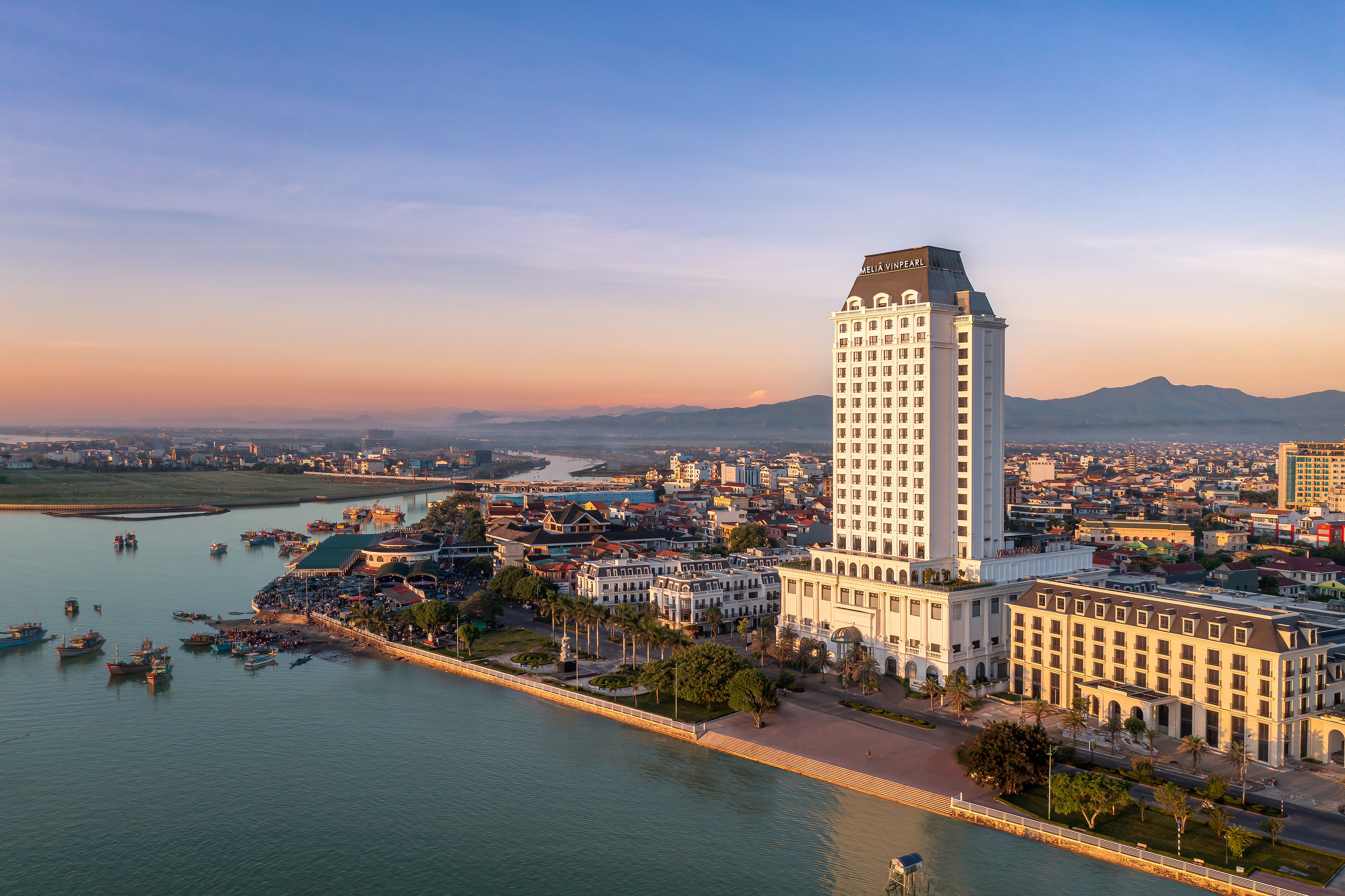 Melia Vinpearl Tuy Hoa hotel, city, river, and boats at sunrise.