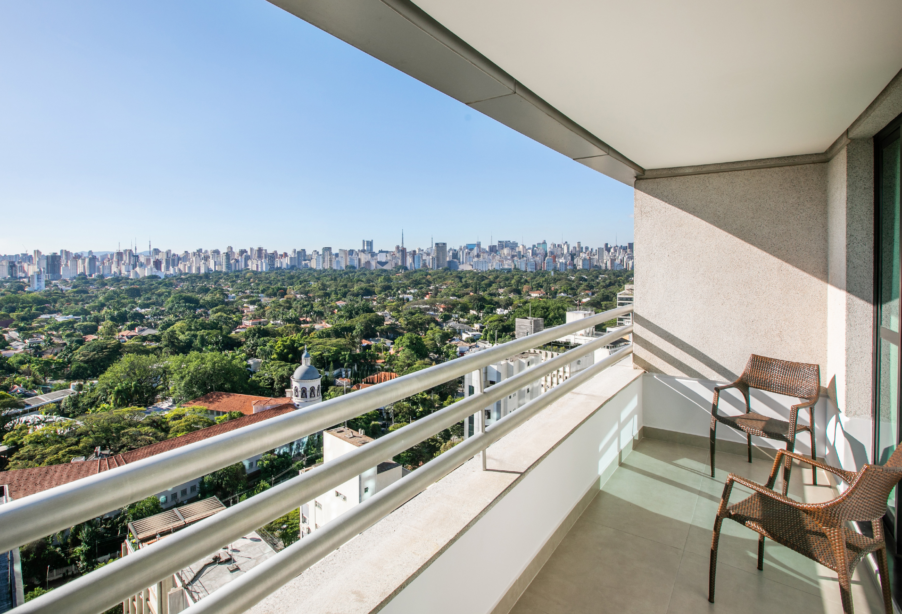 Modern balcony with chairs overlooking a city skyline and green urban landscape.