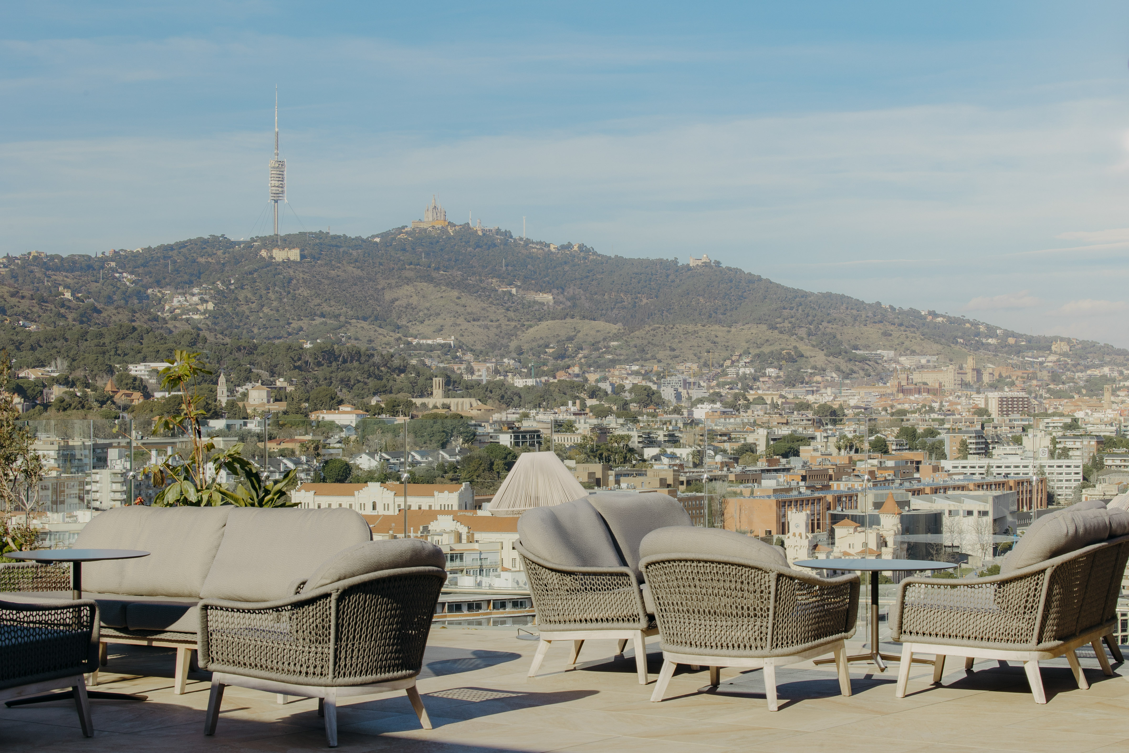 Lounge seating on rooftop terrace overlooking Barcelona skyline, Tibidabo mountain.