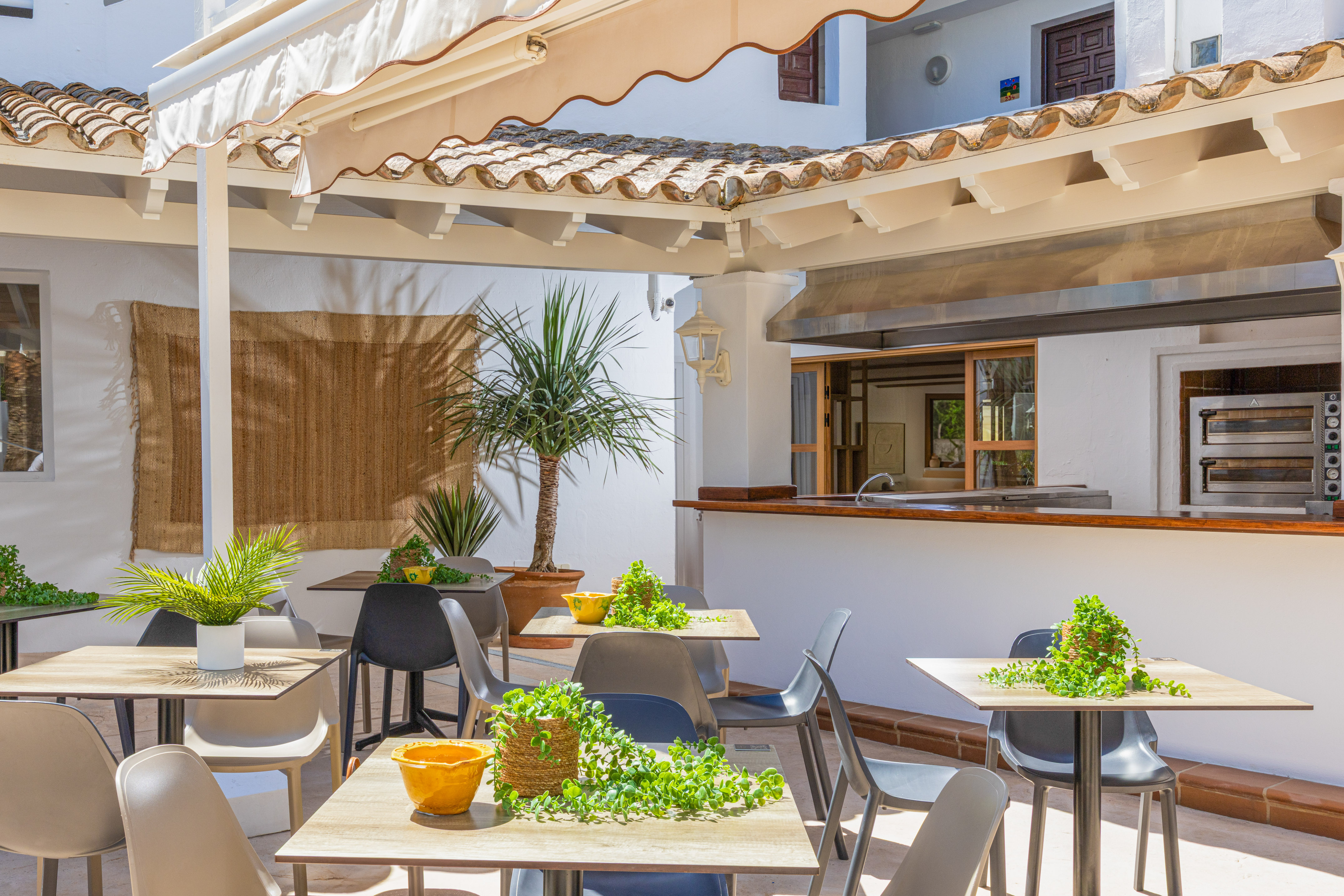 Outdoor restaurant patio with tables, plants, and kitchen bar.