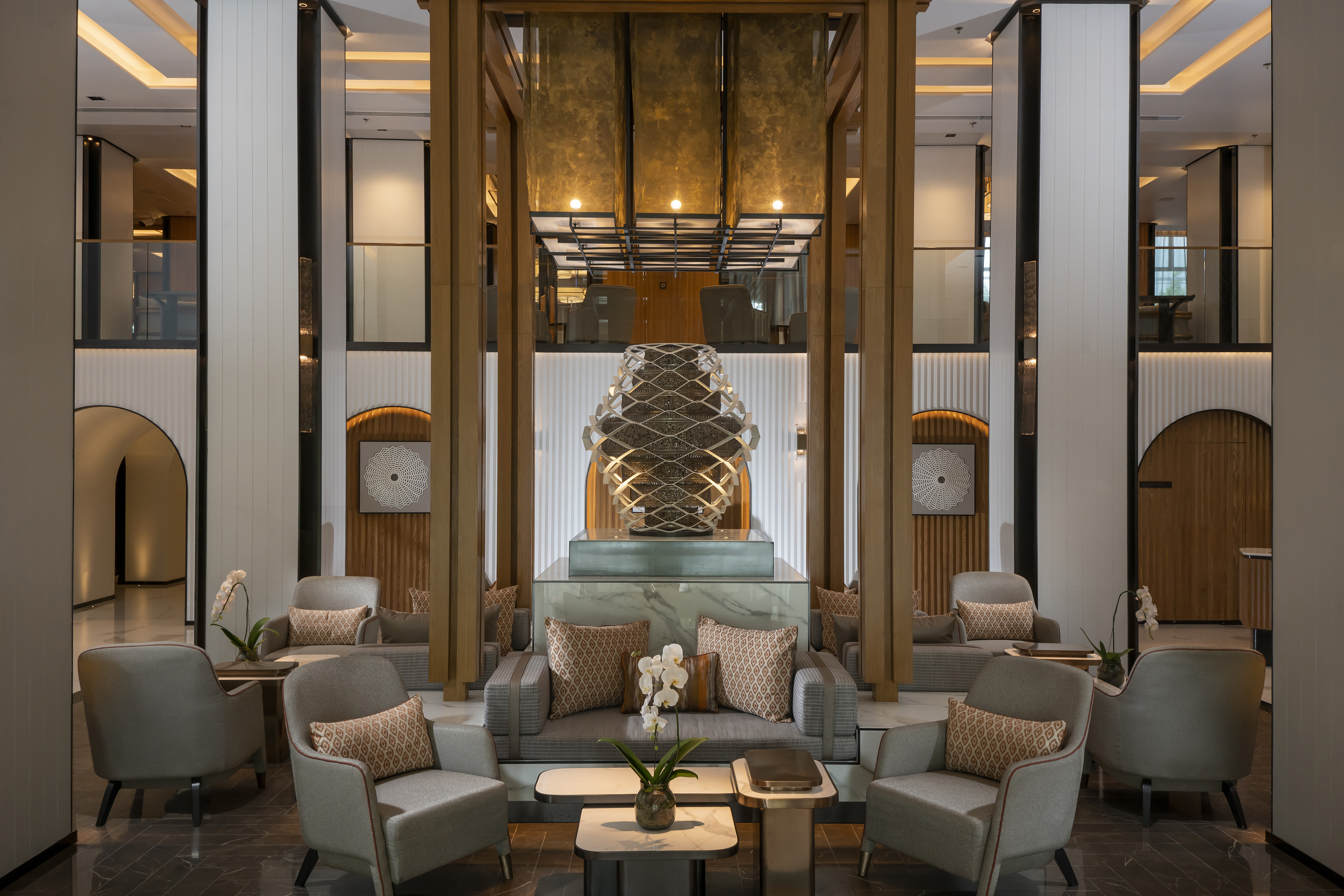 Modern luxury hotel lobby with stylish seating, central art piece, and warm ambiance.
