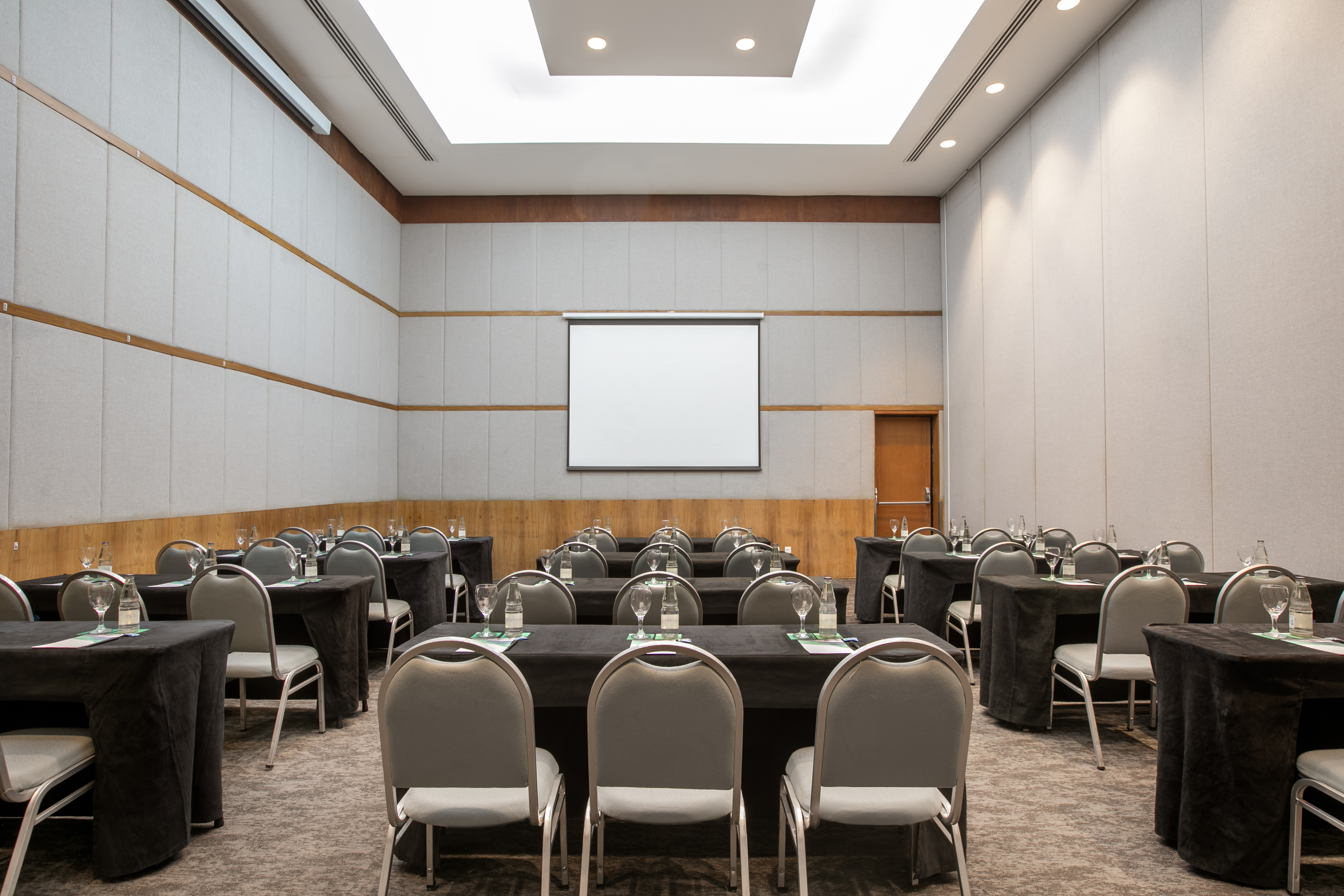 Meeting room with black tables, grey chairs, and a large projector screen.