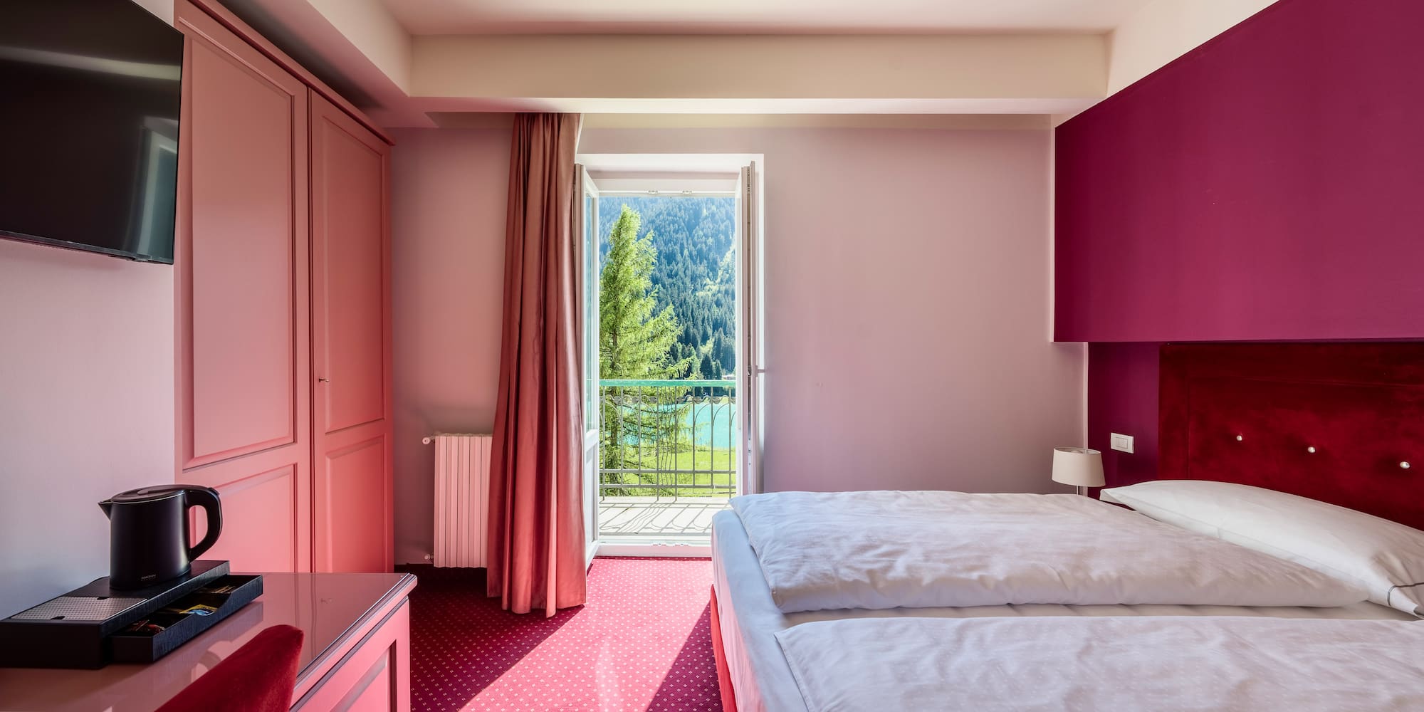 Pink hotel bedroom with twin beds, balcony mountain lake view.