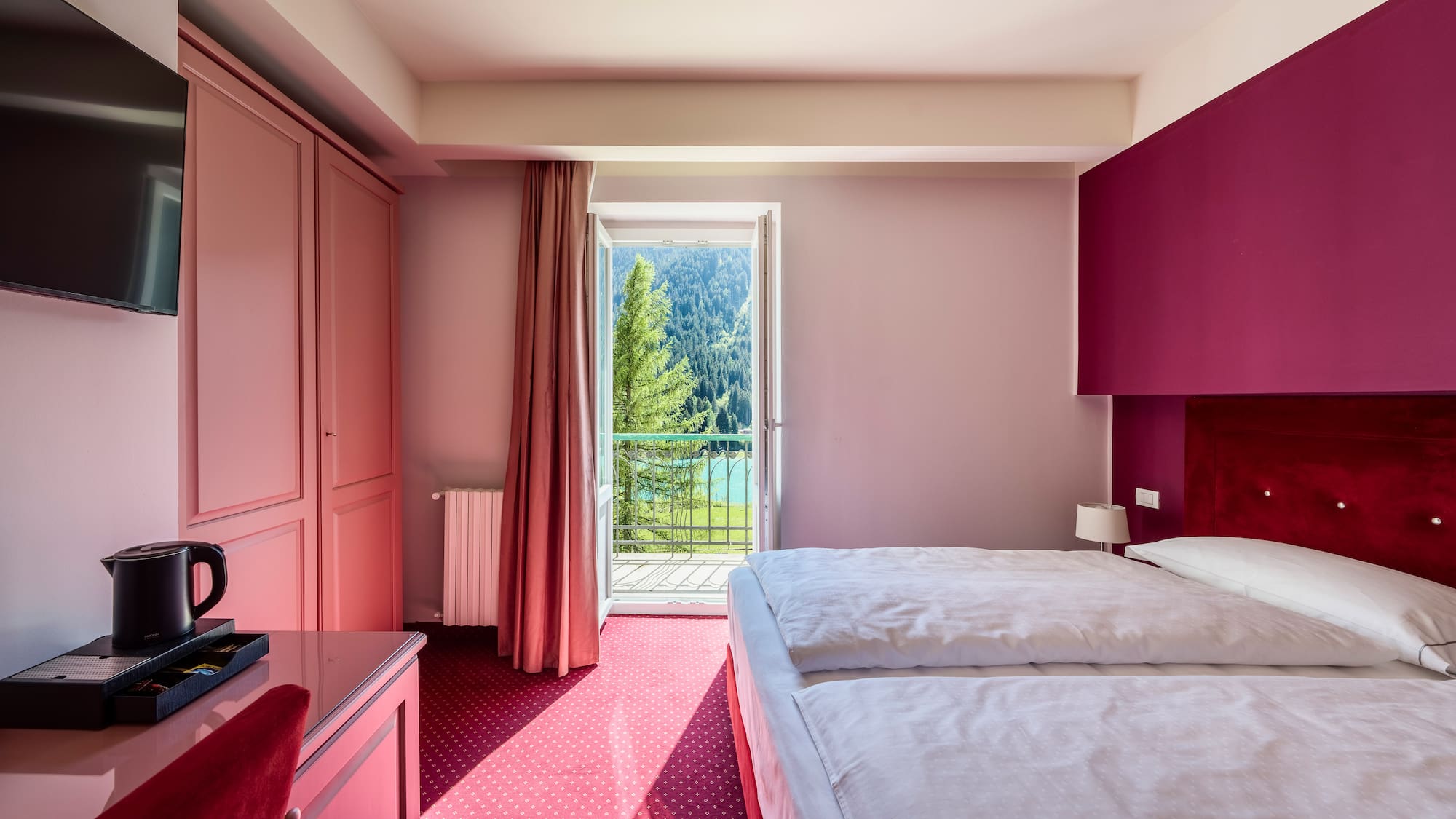 Pink hotel bedroom with twin beds, balcony mountain lake view.