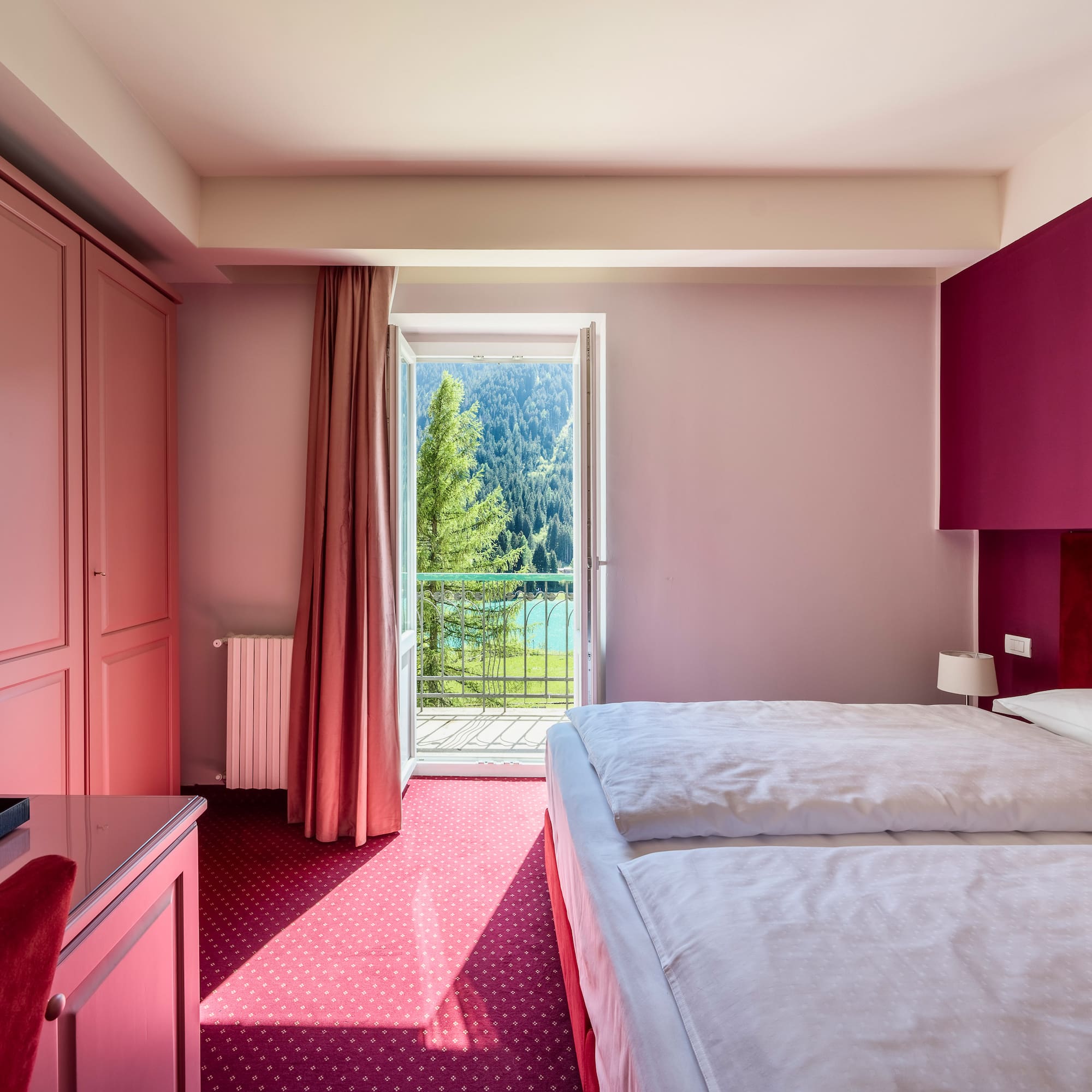 Pink hotel bedroom with twin beds, balcony mountain lake view.