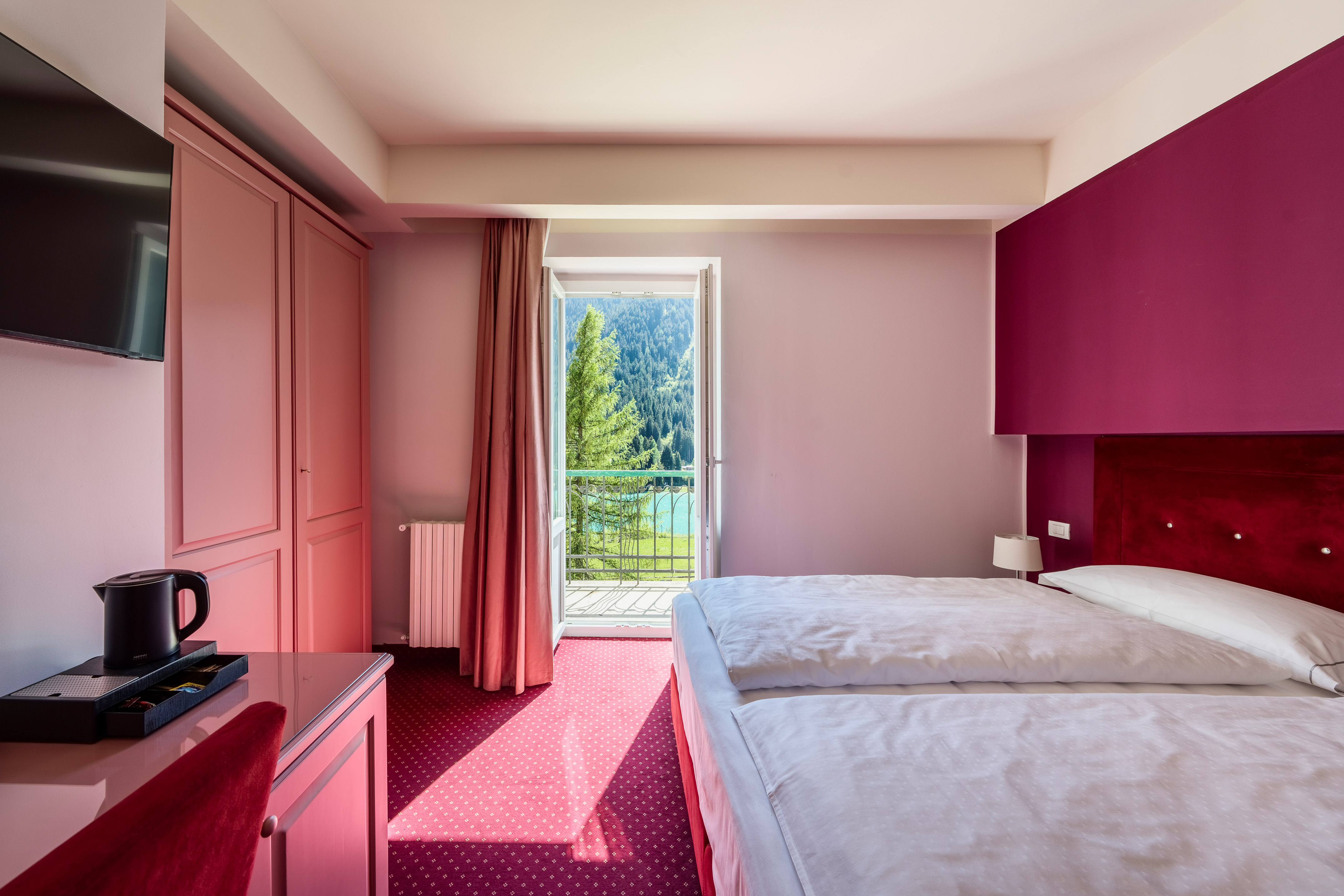 Pink hotel bedroom with twin beds, balcony mountain lake view.
