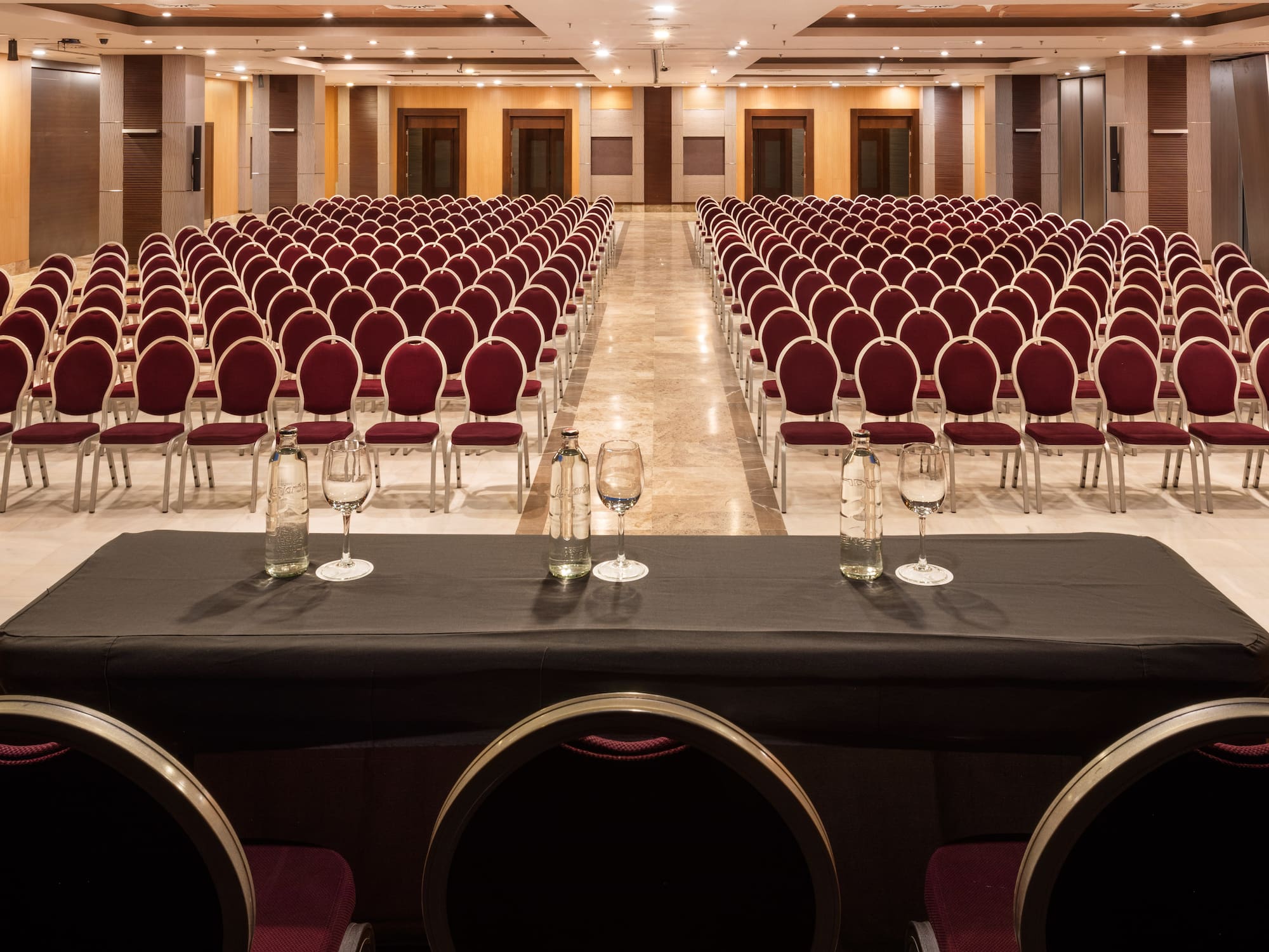 Empty hotel conference room setup with rows of red chairs and speaker table.