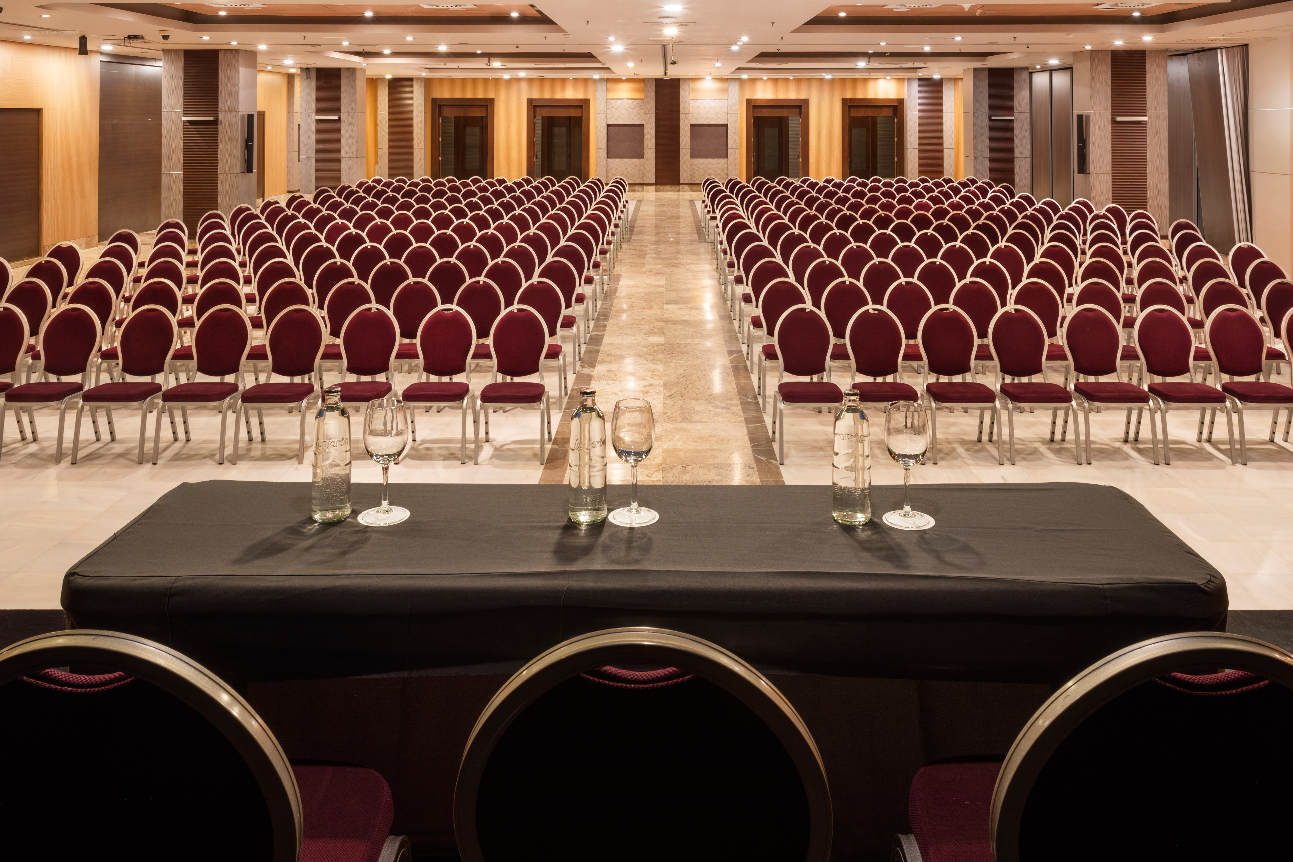 Empty hotel conference room setup with rows of red chairs and speaker table.