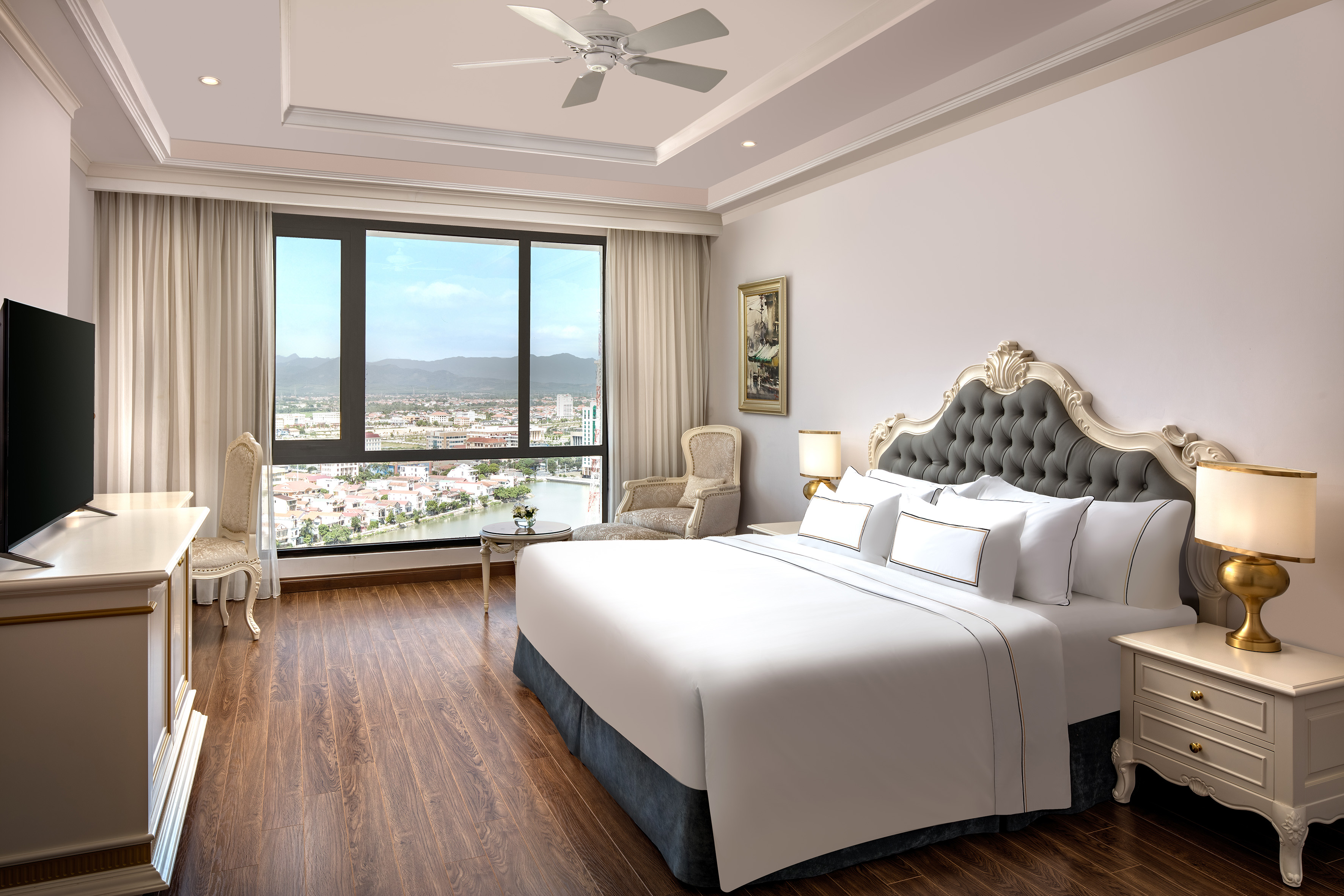 Elegant hotel bedroom with city and river view, large bed, and wood flooring.