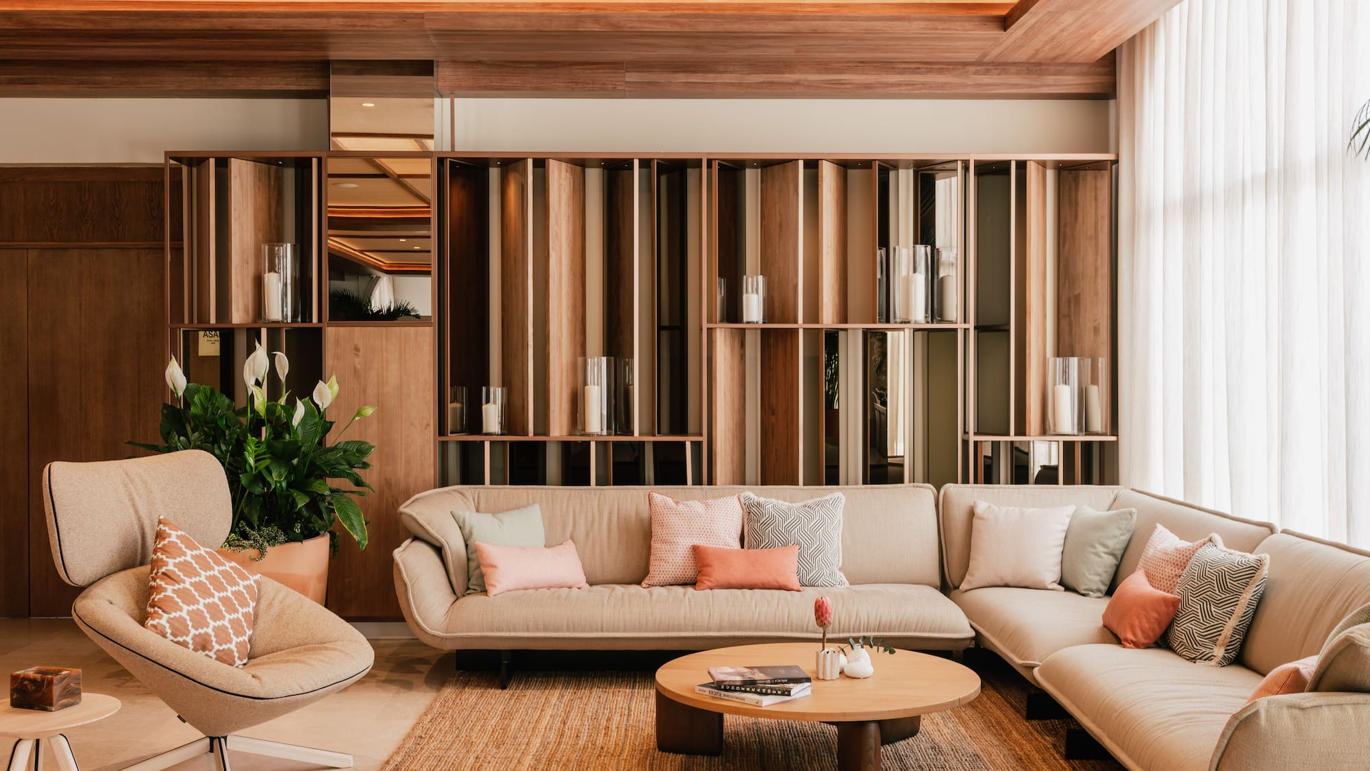 Modern neutral lounge with beige sofa, wooden wall, coffee table, and plant.