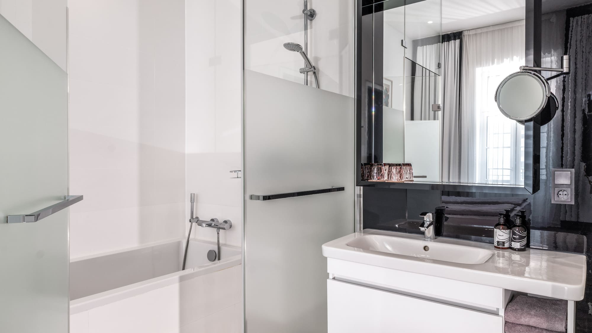 Clean, modern hotel bathroom with white bathtub, glass shower, and vanity.