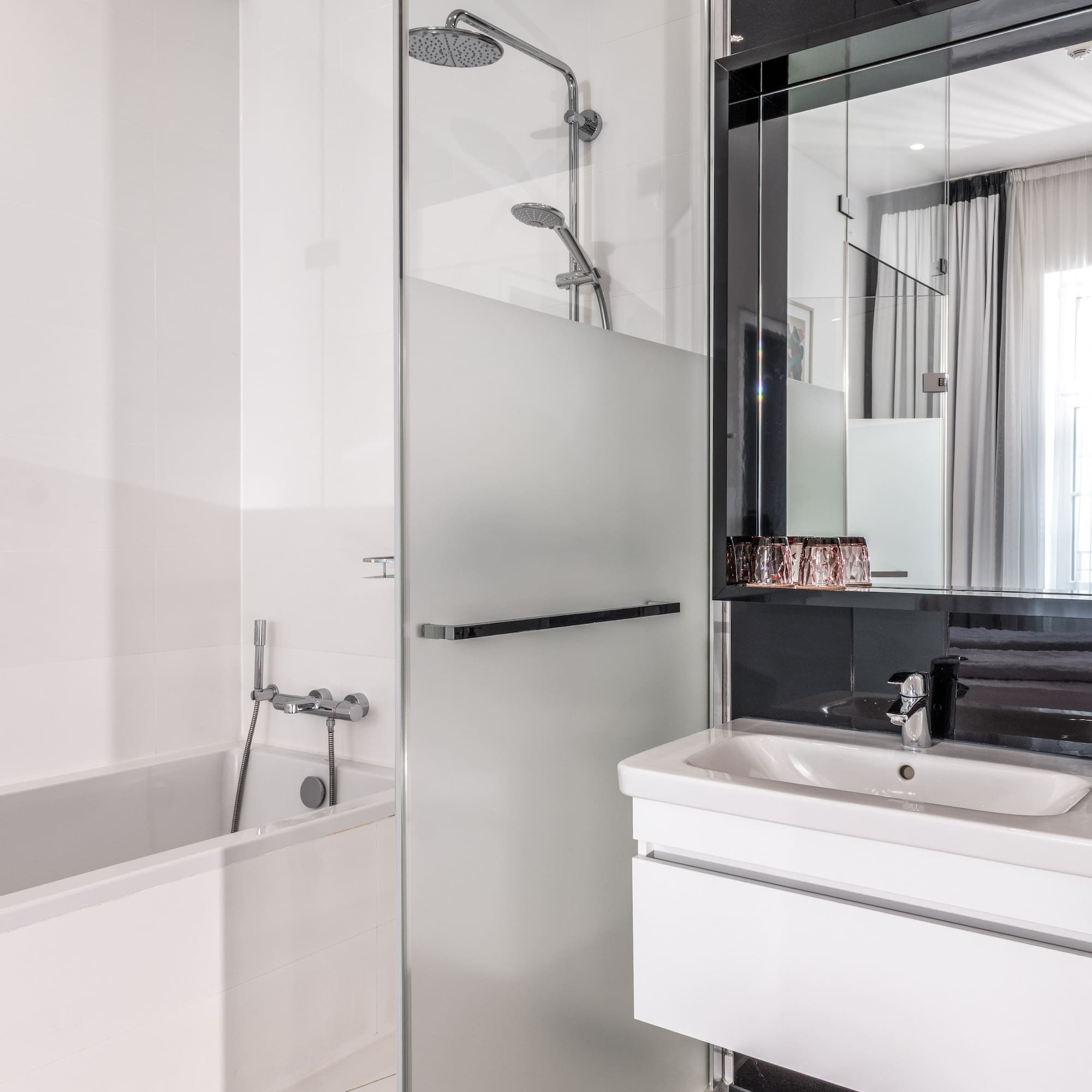 Clean, modern hotel bathroom with white bathtub, glass shower, and vanity.