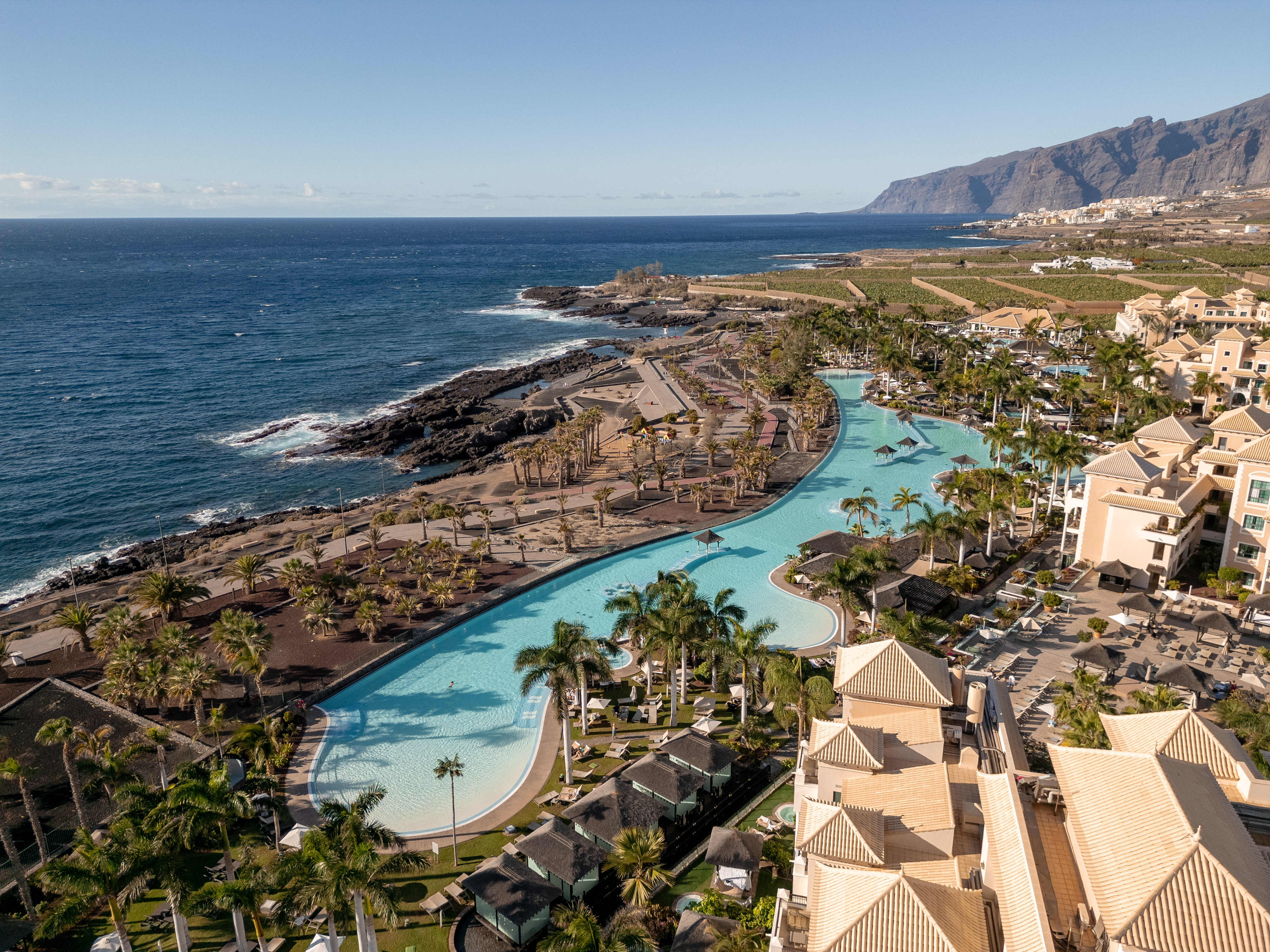 Tenerife resort with winding lagoon pool, palm trees, ocean, and cliffs.