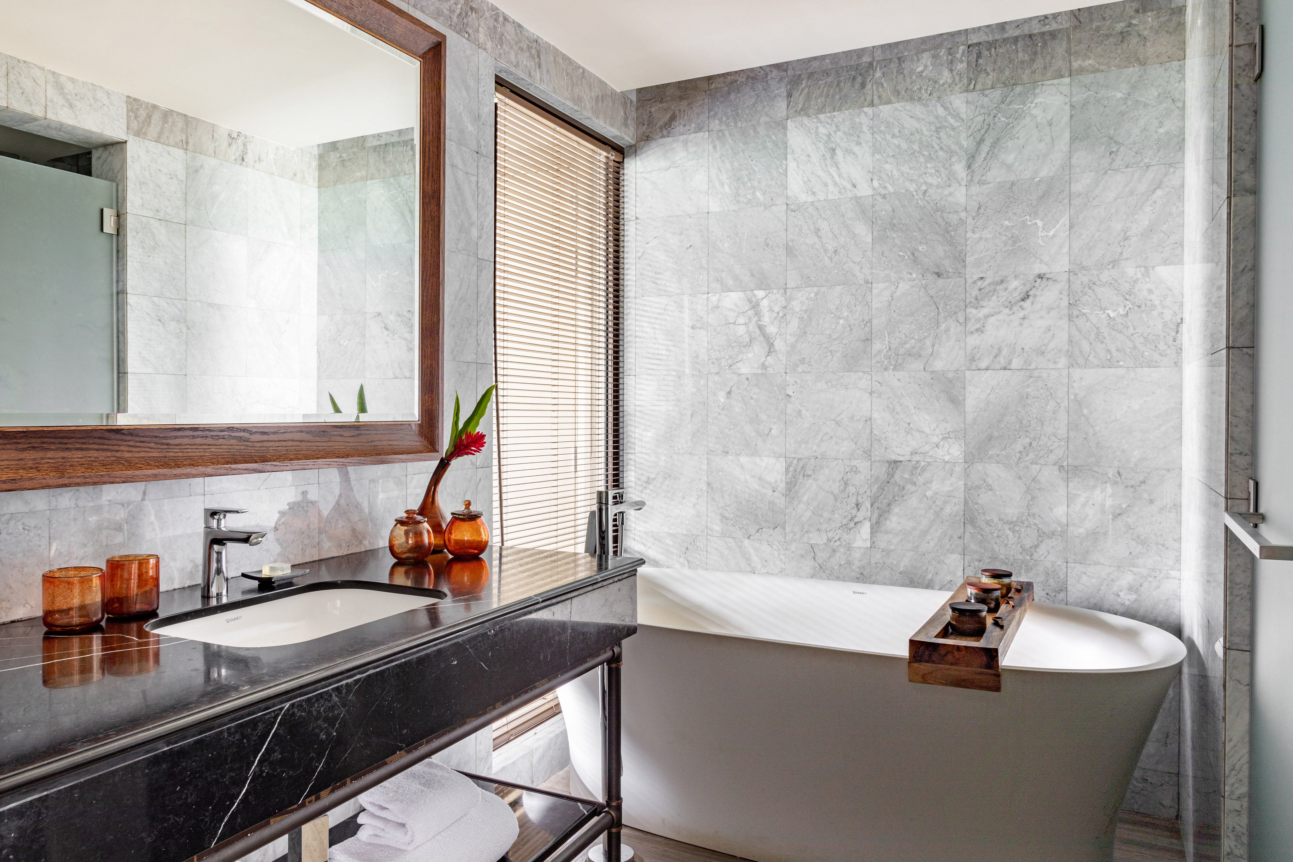 Modern gray marble bathroom with freestanding tub, black vanity, and mirror.