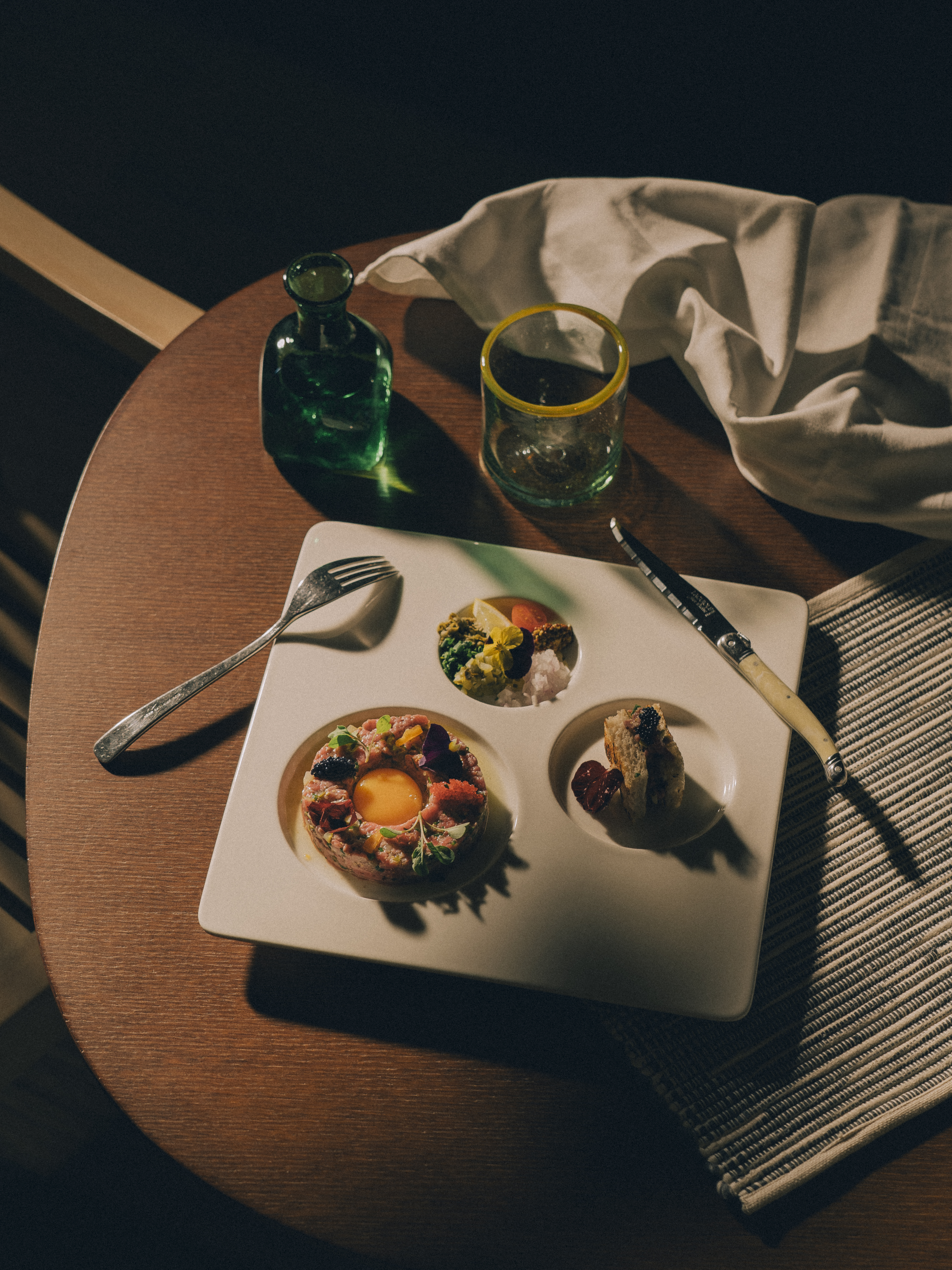Steak tartare with egg yolk, caviar, and sides on a modern tasting plate.