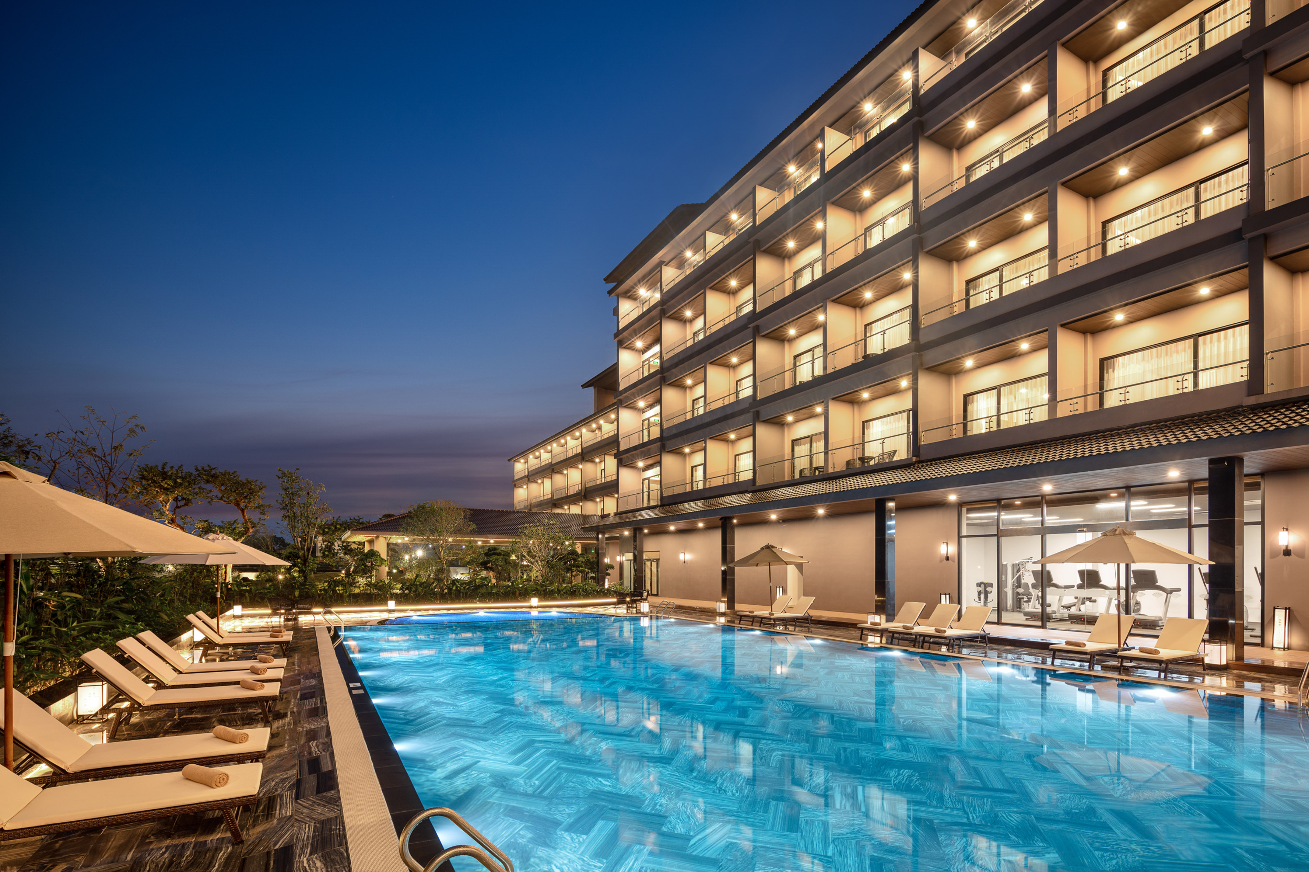 Modern resort hotel with illuminated outdoor pool and lounge chairs at dusk.