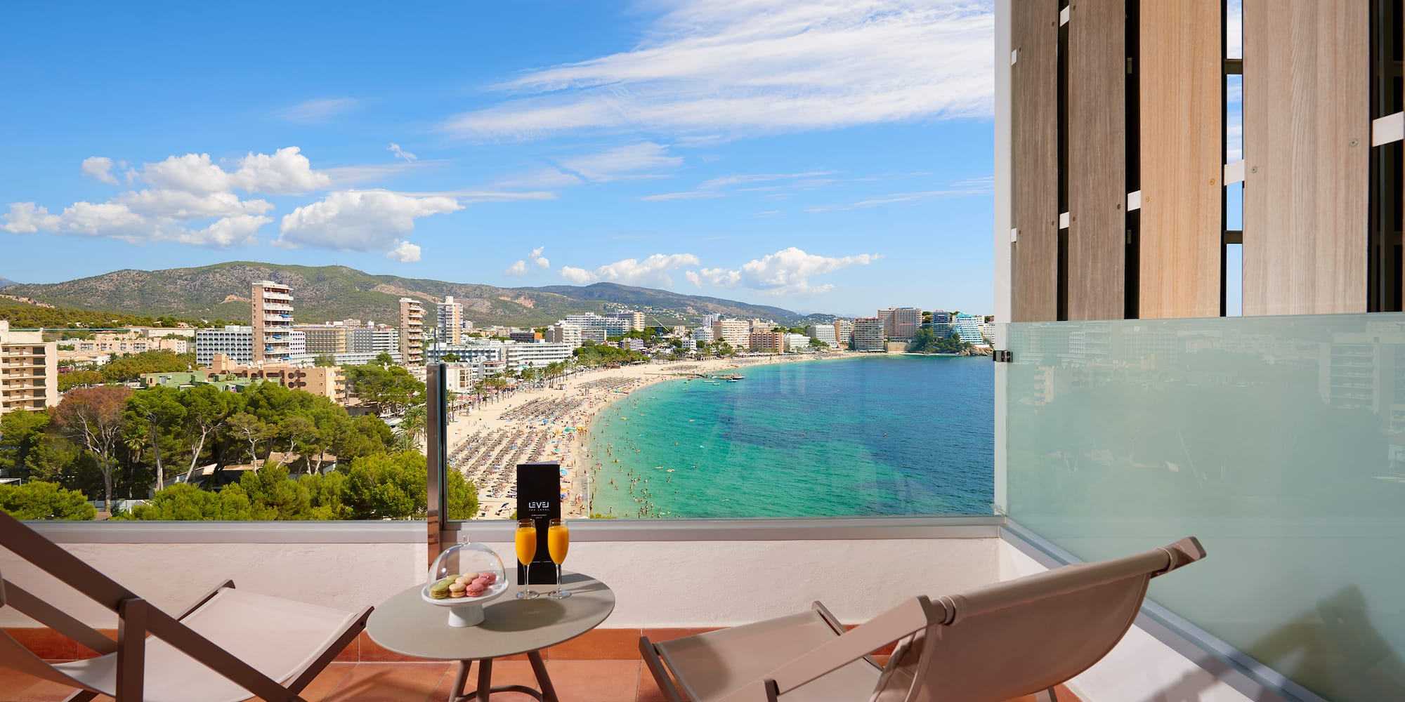 Ocean view balcony with beach, coastal city, mountains. Drinks and lounge chairs.