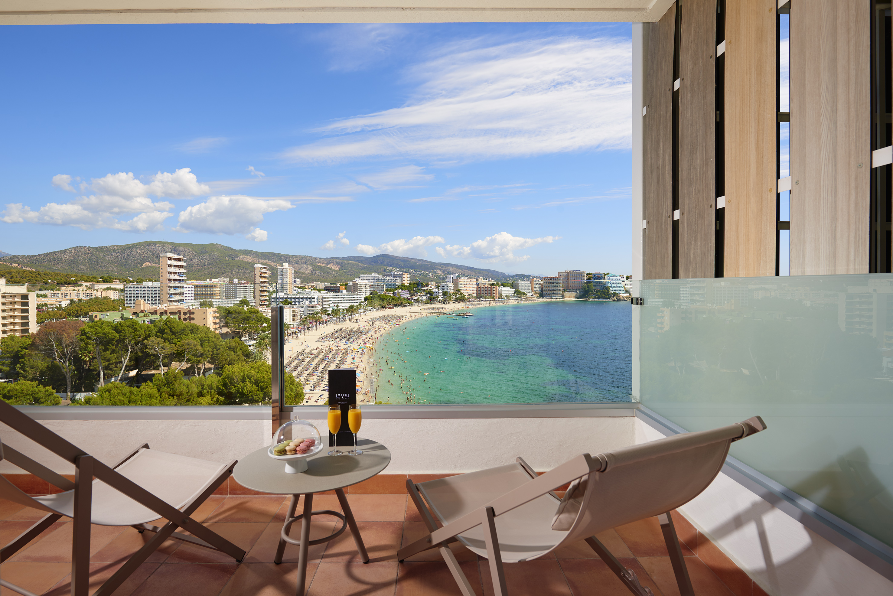 Ocean view balcony with beach, coastal city, mountains. Drinks and lounge chairs.
