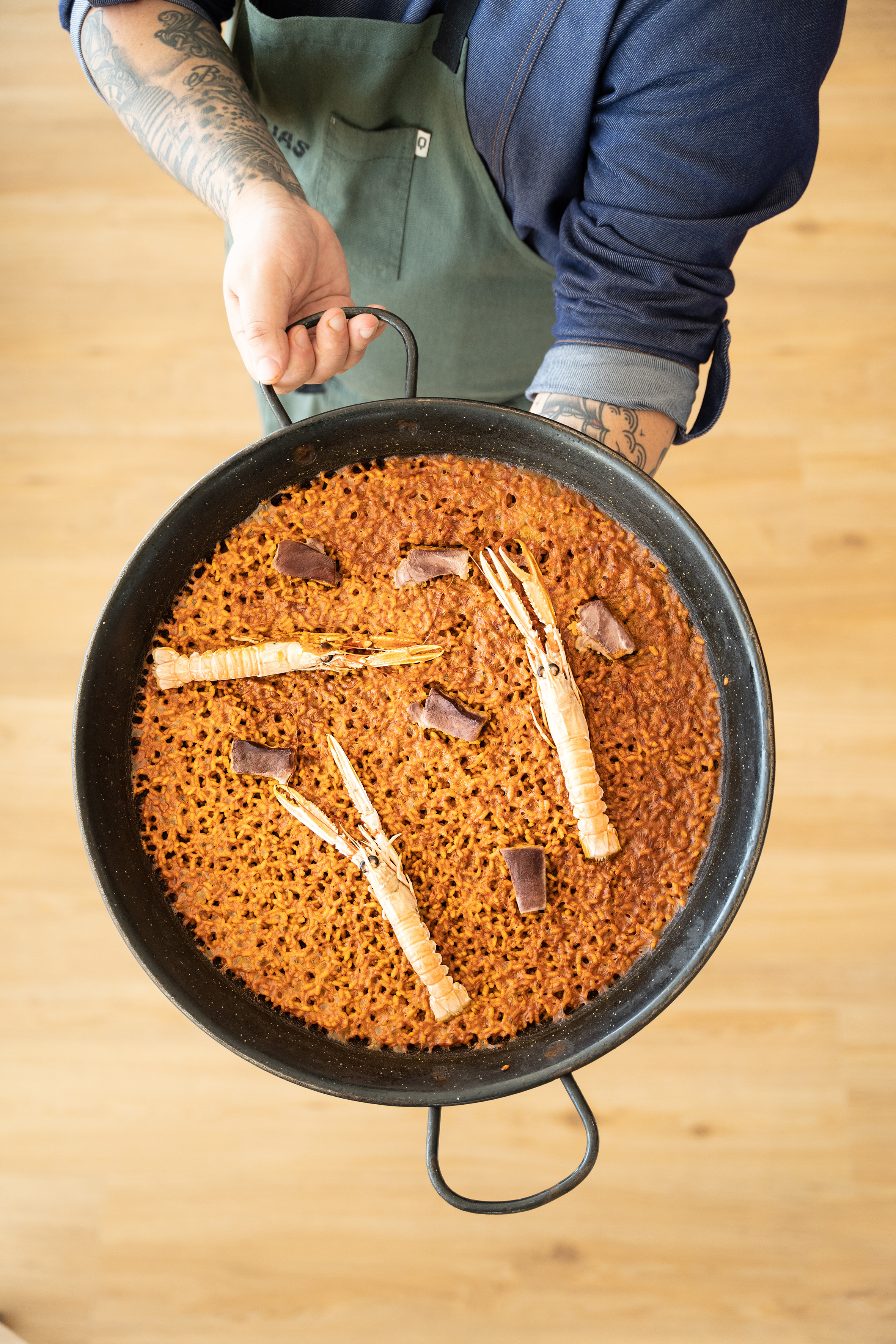 Overhead view of chef presenting seafood paella with langoustines and meat.