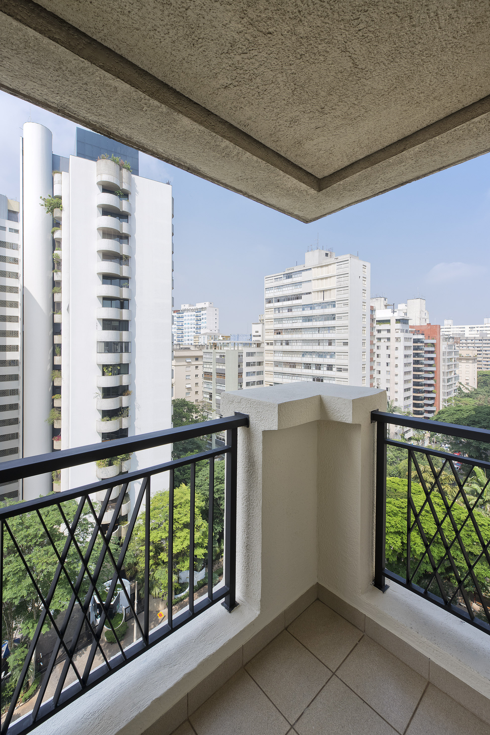 Balcony view of modern city apartments, black railing, and green trees.