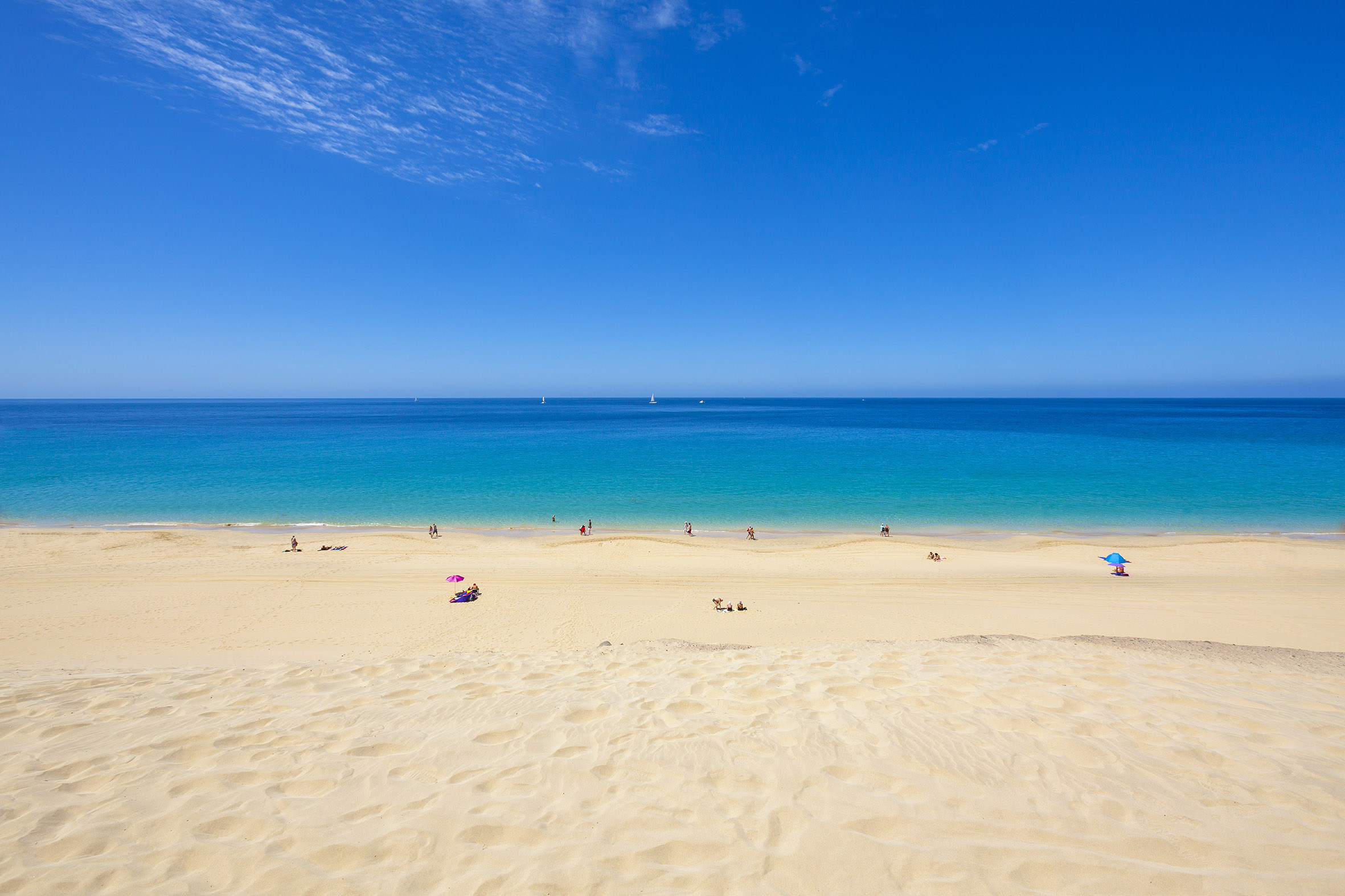 Golden sand beach, turquoise ocean, blue sky, people, distant sailboats.