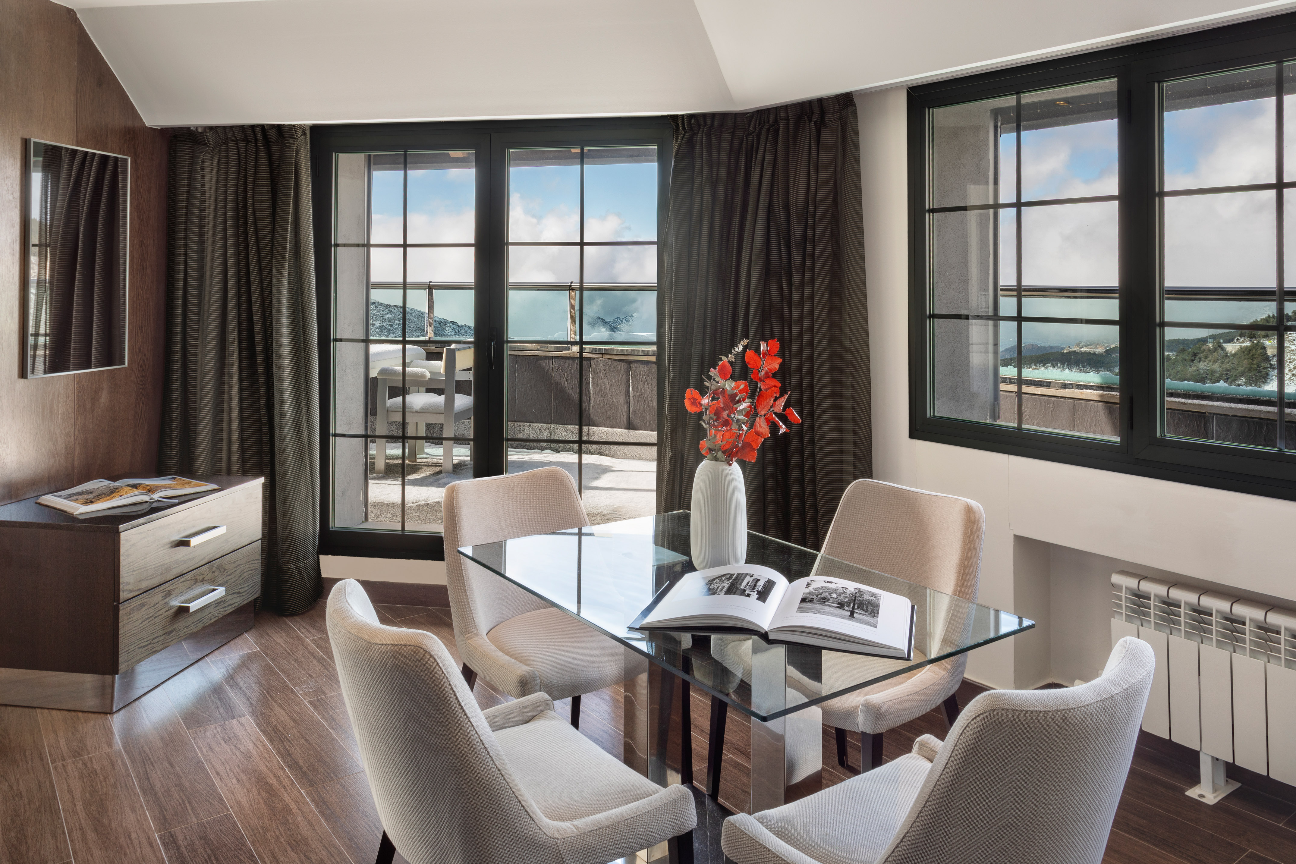 Modern living area with glass table, balcony, and snowy mountain view.