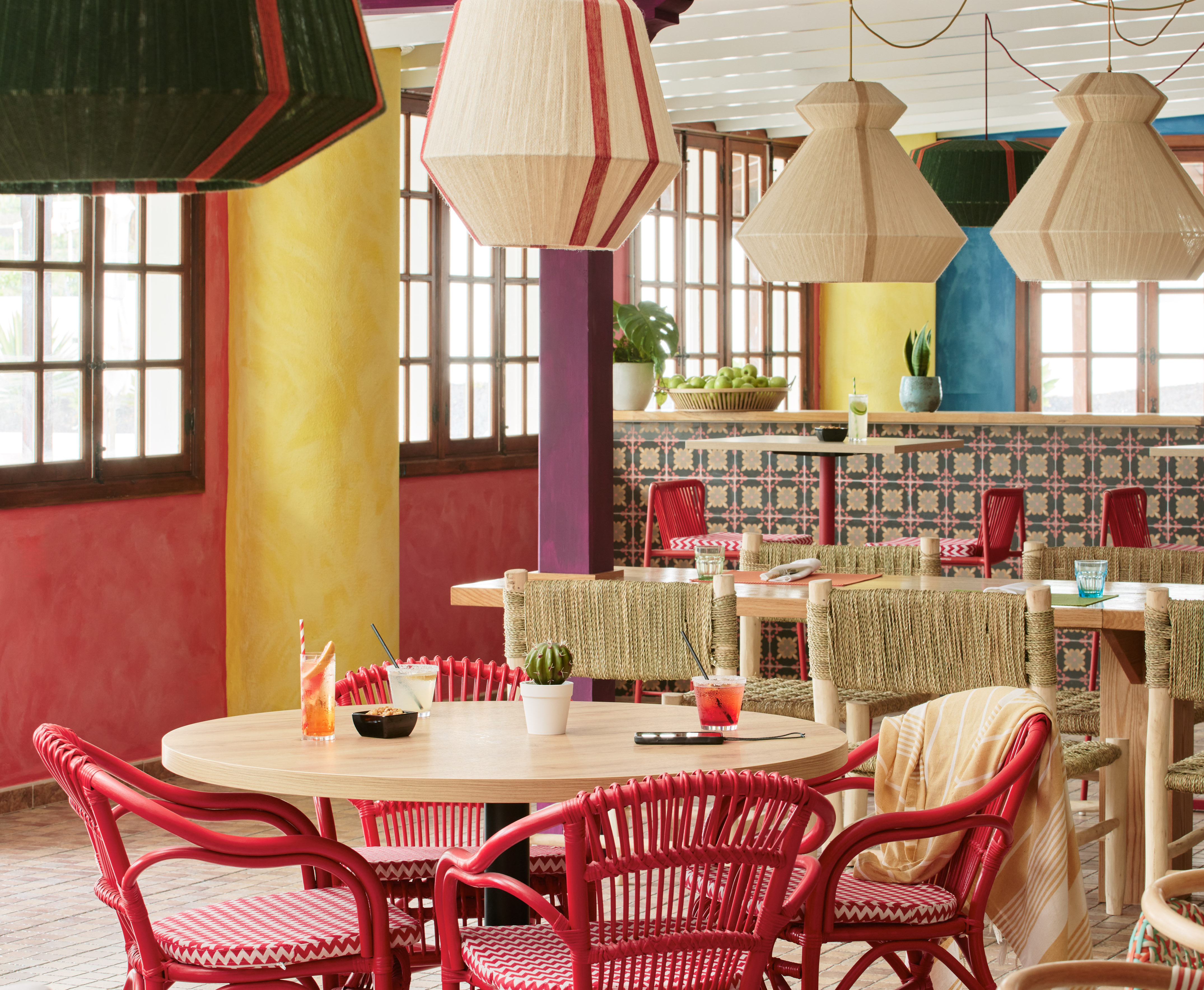 Vibrant cafe interior with red rattan chairs, wooden tables, and woven lights.