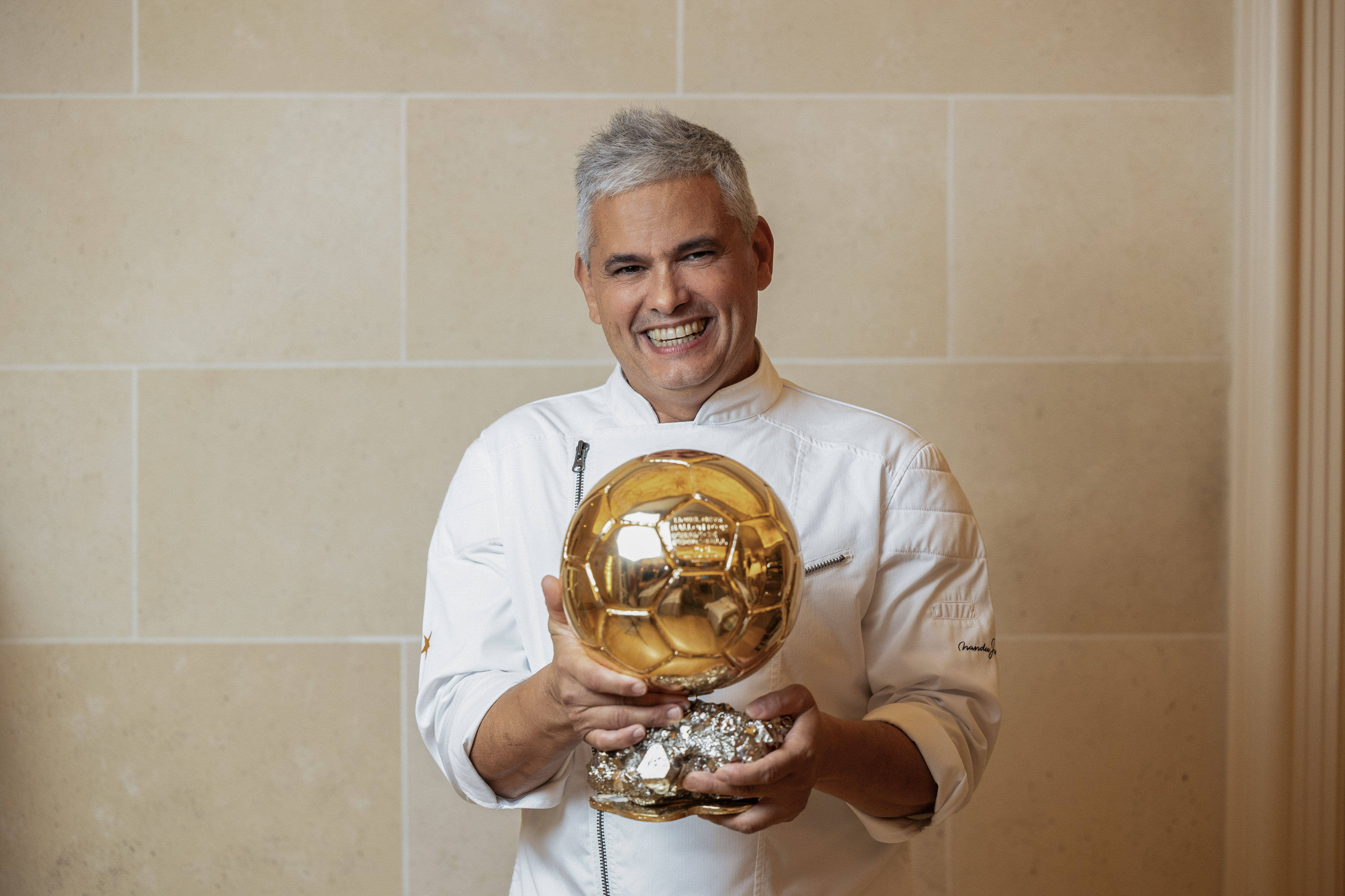 Chef smiling, holding a golden football award trophy.