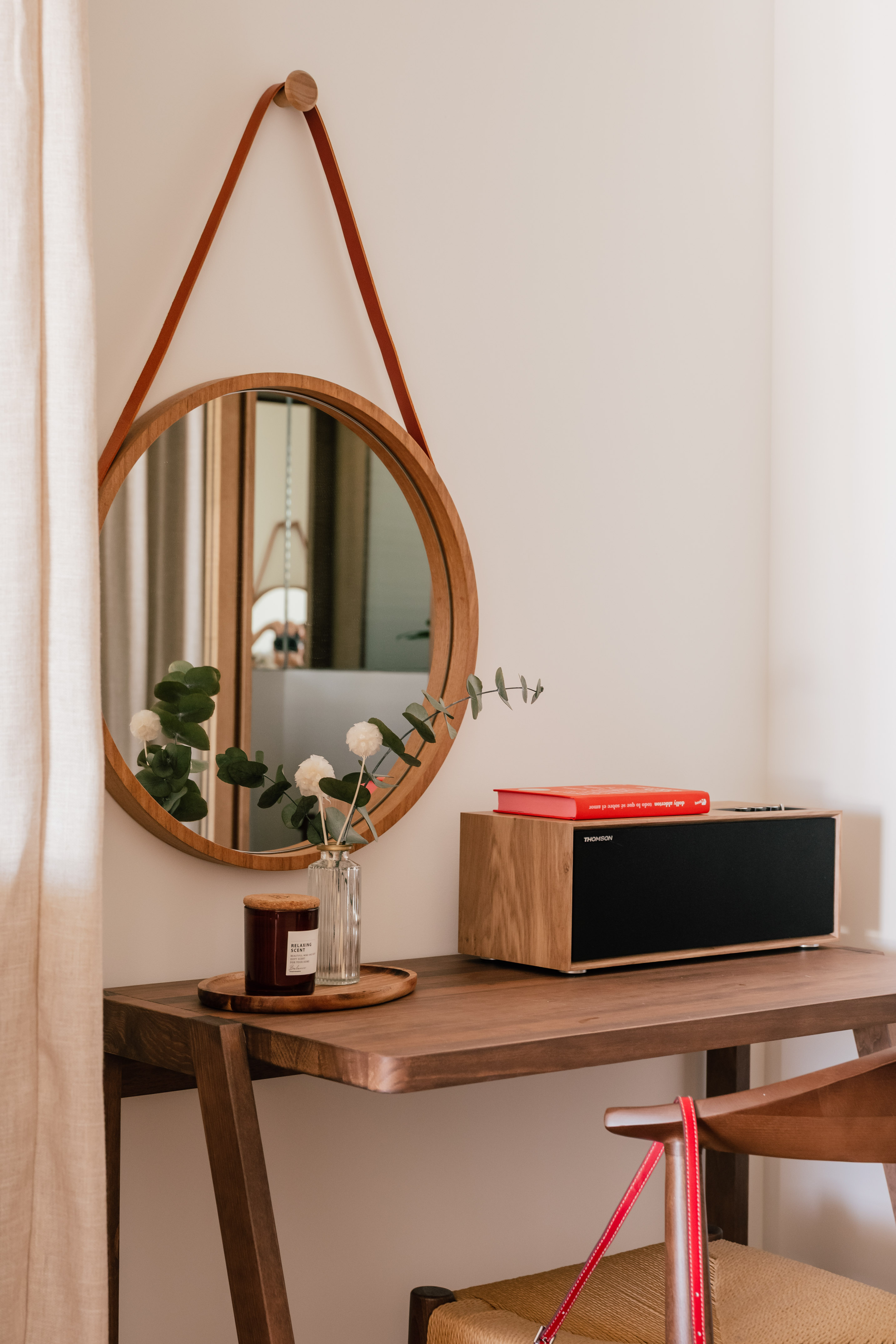 Round wooden mirror, leather strap, and console table with speaker, candle, diffuser.