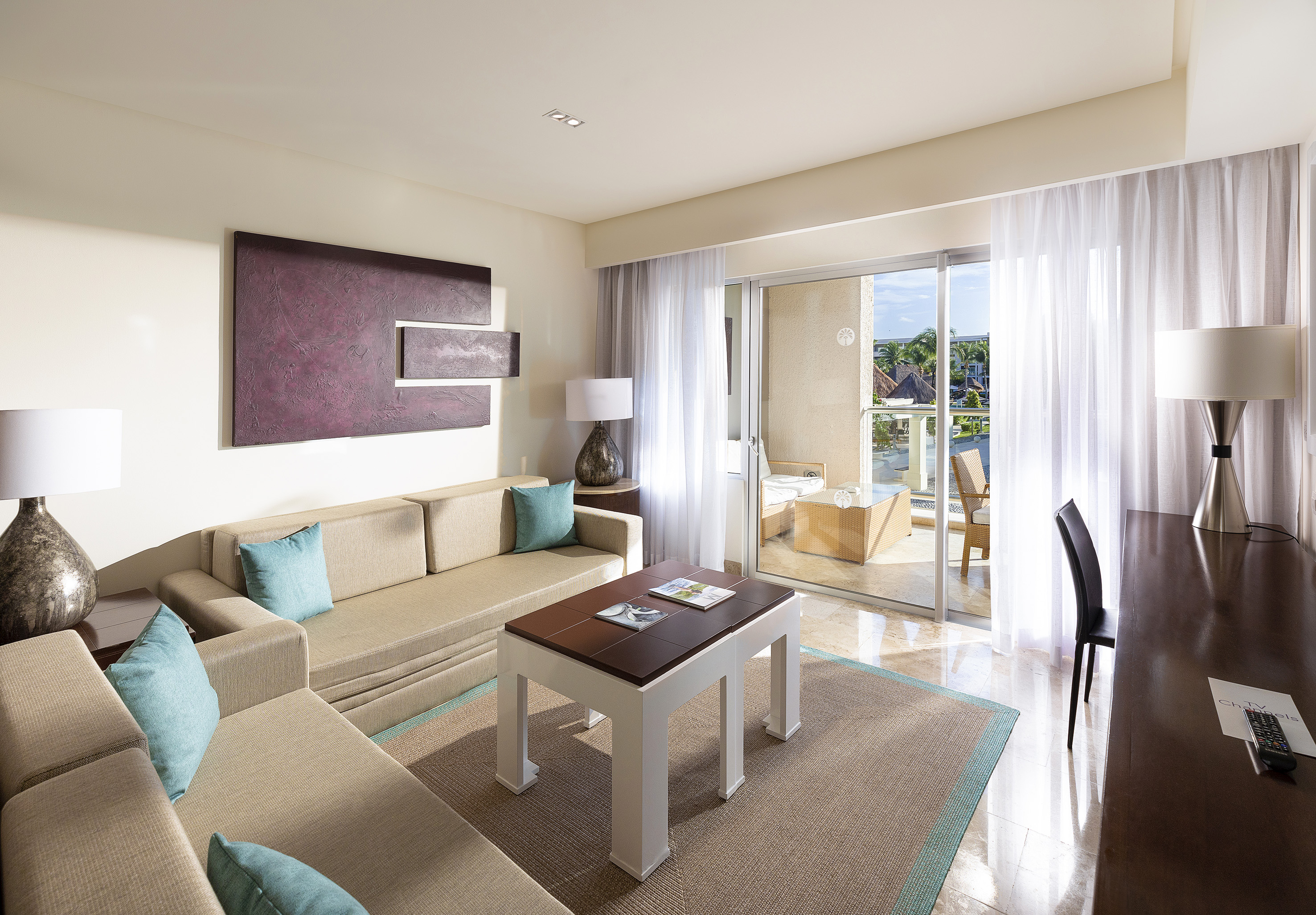 Modern hotel living room with beige sofa, coffee table, and balcony access.