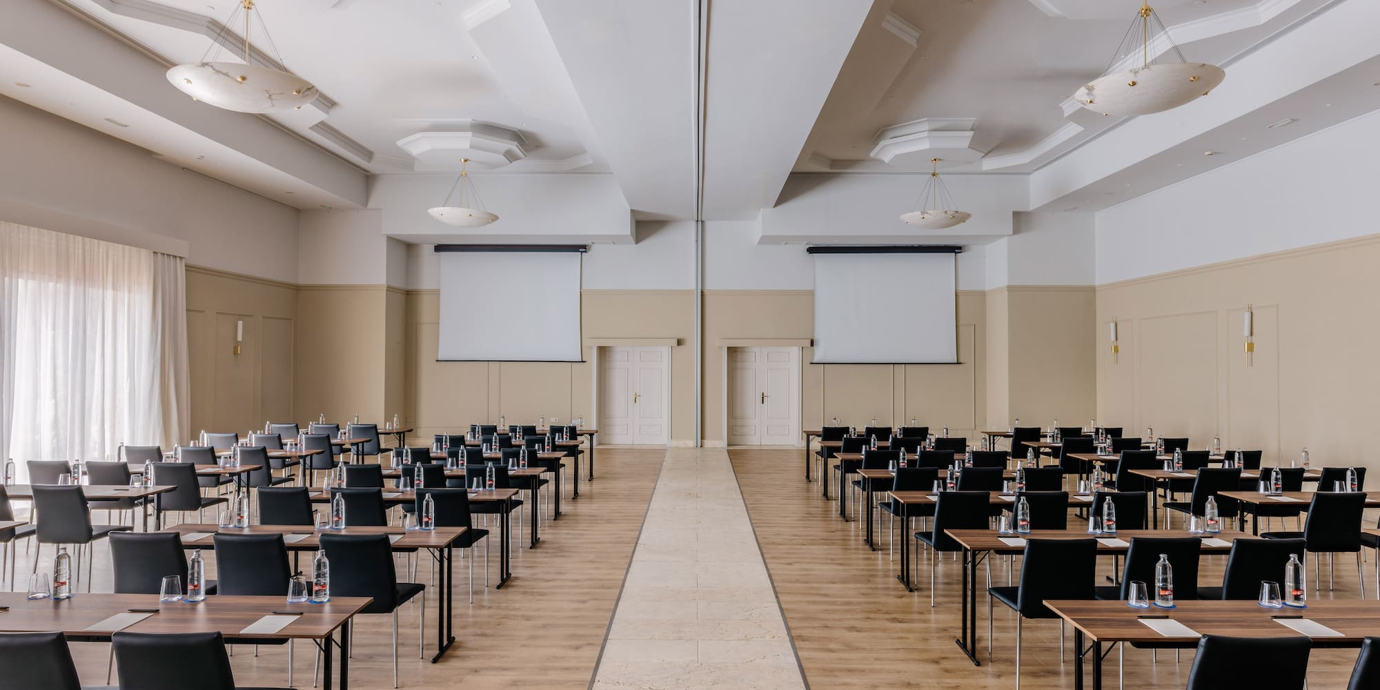 Empty conference room with tables, chairs, two screens, and central aisle.
